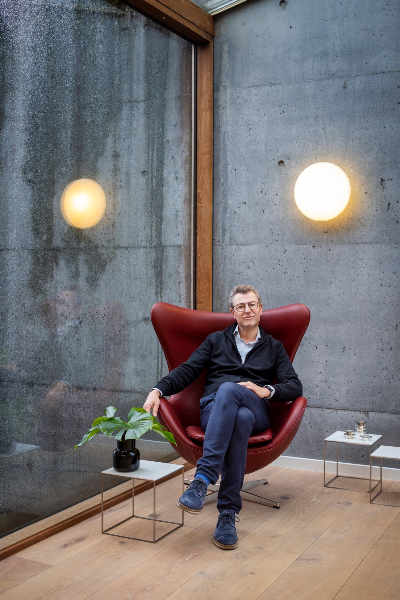 Josef Kaiser, CEO of Fritz Hansen, sitting in a red chair against concrete walls with circular light fixtures