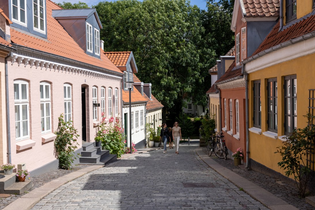 Cobblestone street lined with colorful traditional Danish houses and red tile roofs in Odense