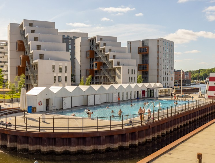 Modern outdoor swimming pool built on waterfront platform with contemporary apartment buildings in background