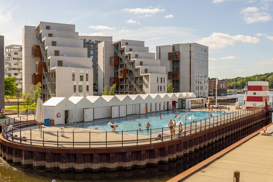 Modern outdoor swimming pool built on waterfront platform with contemporary apartment buildings in background