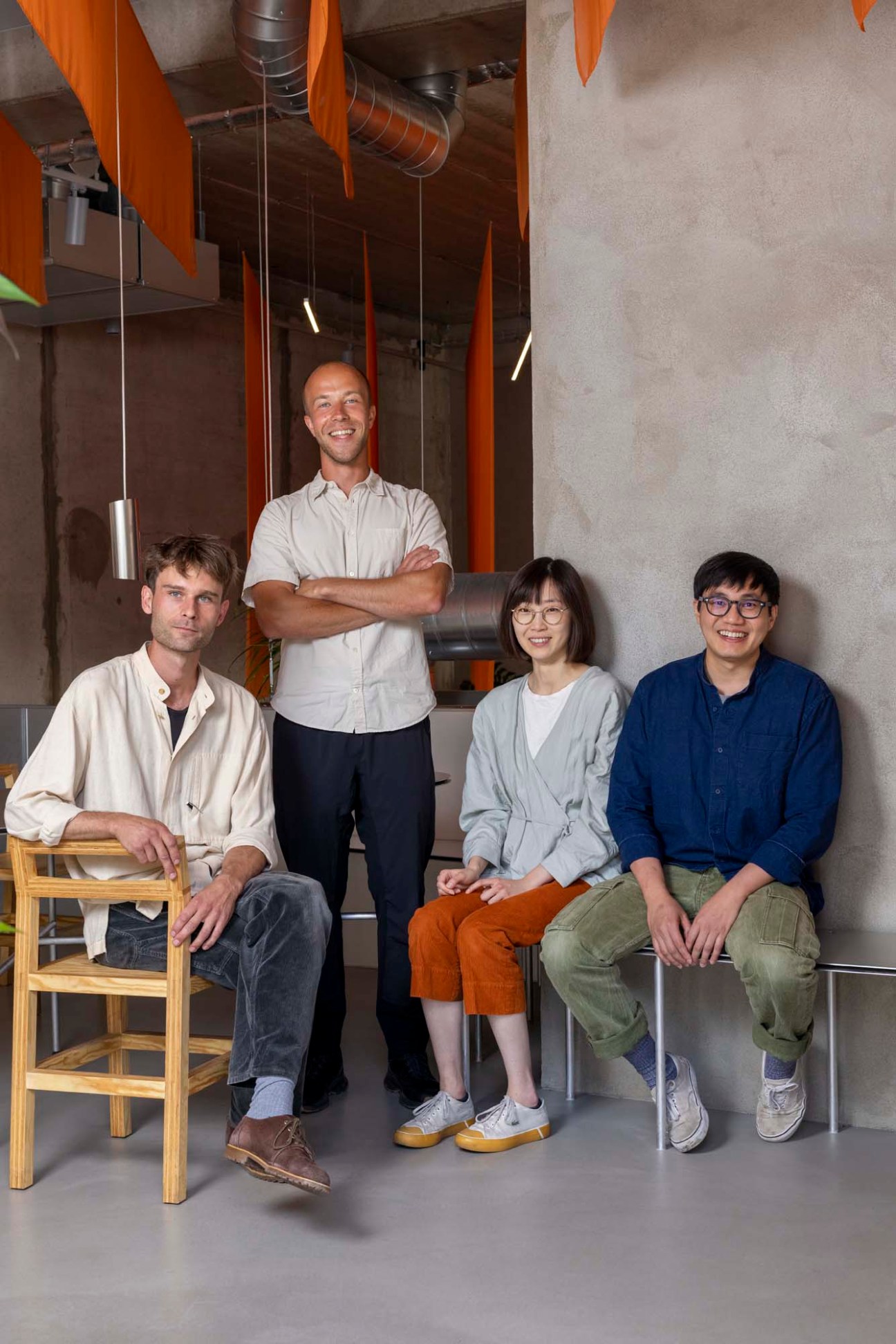 Benas Burdulis standing with three colleagues in the modern interior of Kona restaurant with orange architectural details