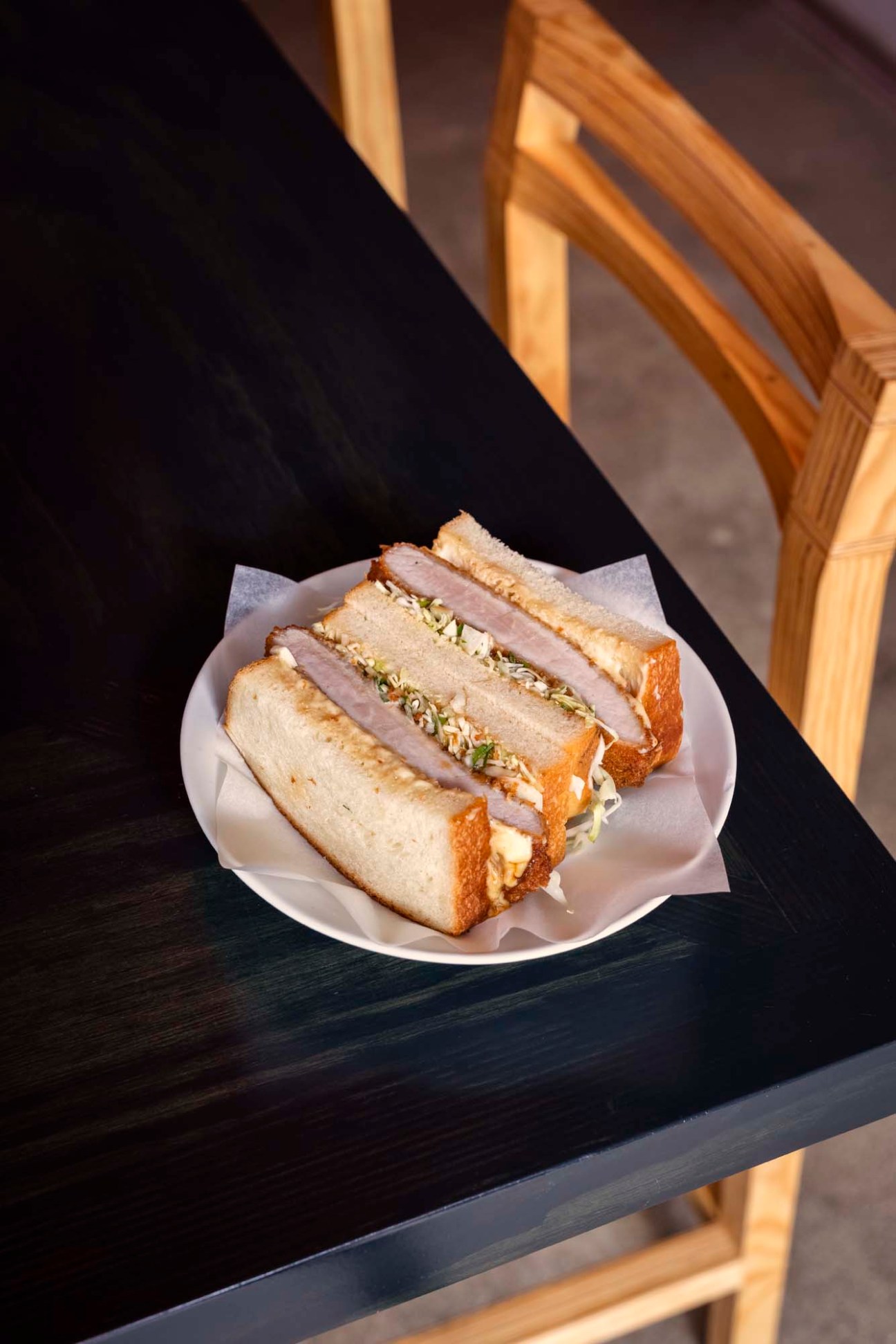 Katsu sando sandwich with crispy breaded cutlet and garnish on white plate.