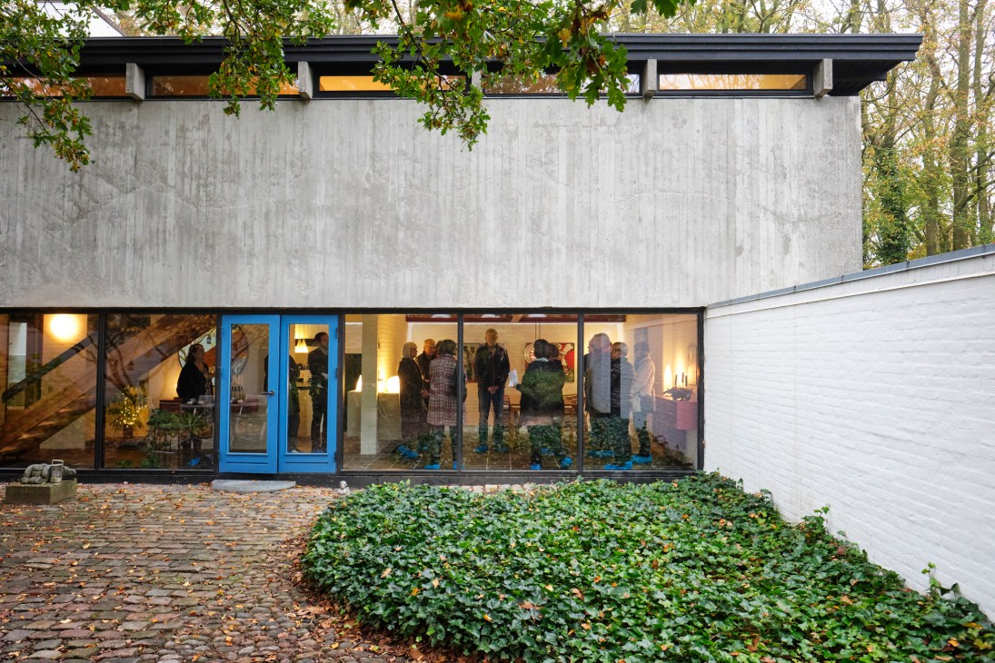 Exterior of Knud Friis' brutalist house in Aarhus with visitors visible through large windows.