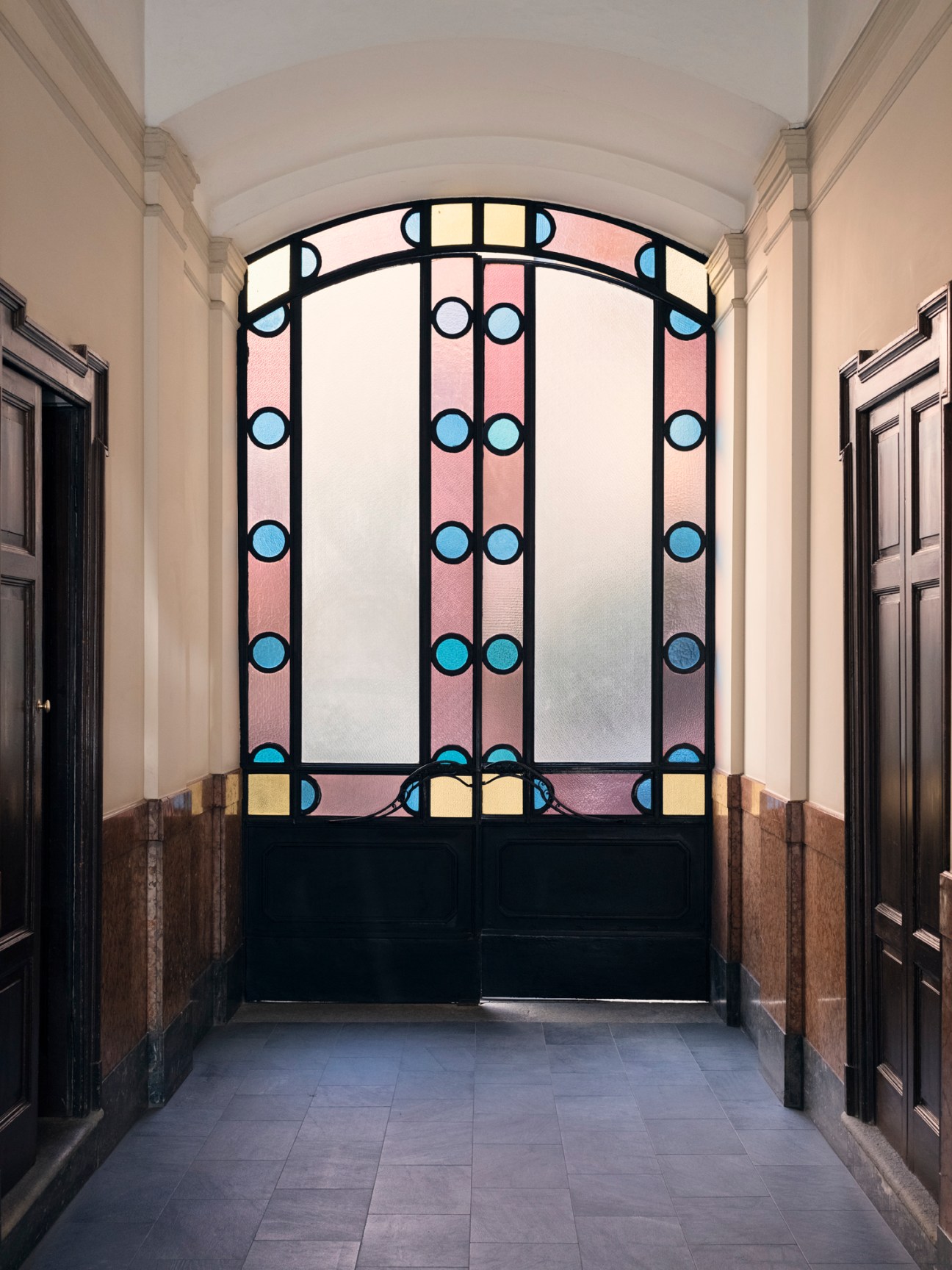 Art nouveau stained glass window with geometric pattern and colorful panels in an elegant arched hallway