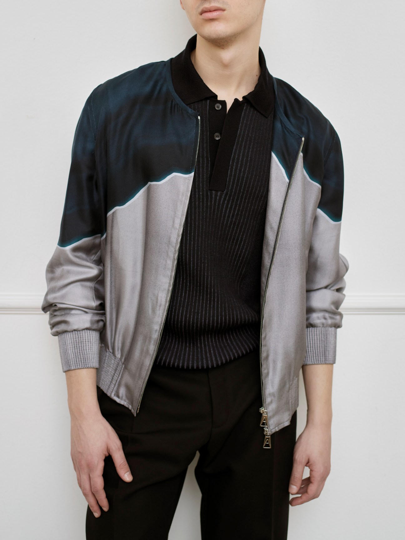 Man wearing colorblock jacket with navy, grey and white panels and black ribbed polo shirt