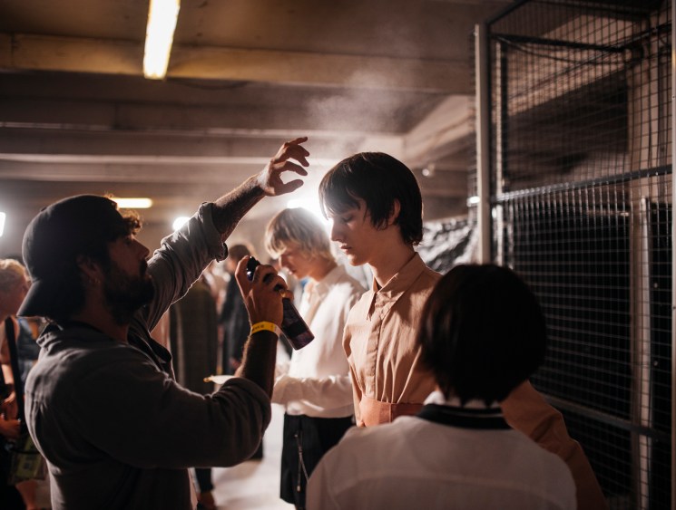 Behind-the-scenes view of styling team preparing looks and hanging garments backstage at fashion show
