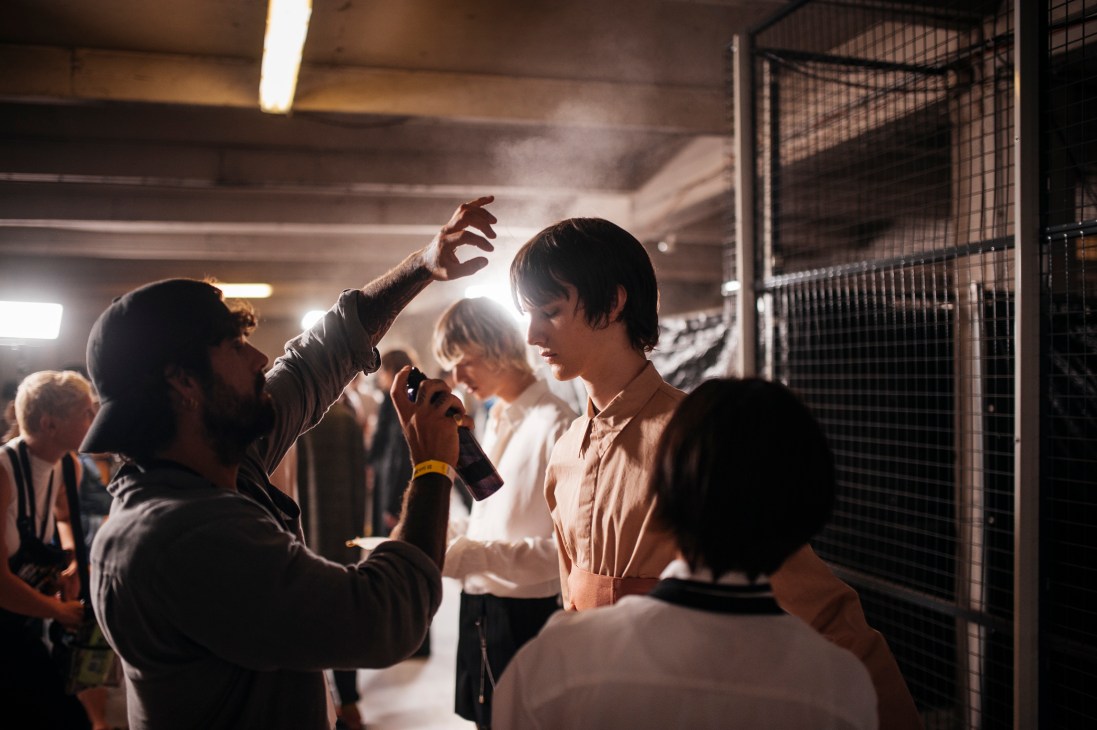 Behind-the-scenes view of styling team preparing looks and hanging garments backstage at fashion show