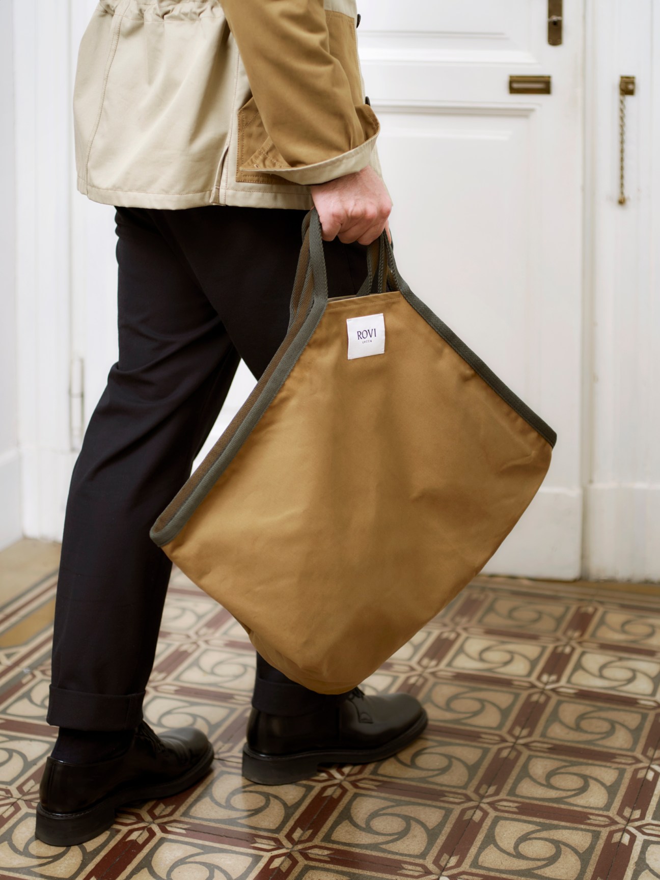 Man carrying a tan leather tote bag with grey handles by Rovi Lucca.