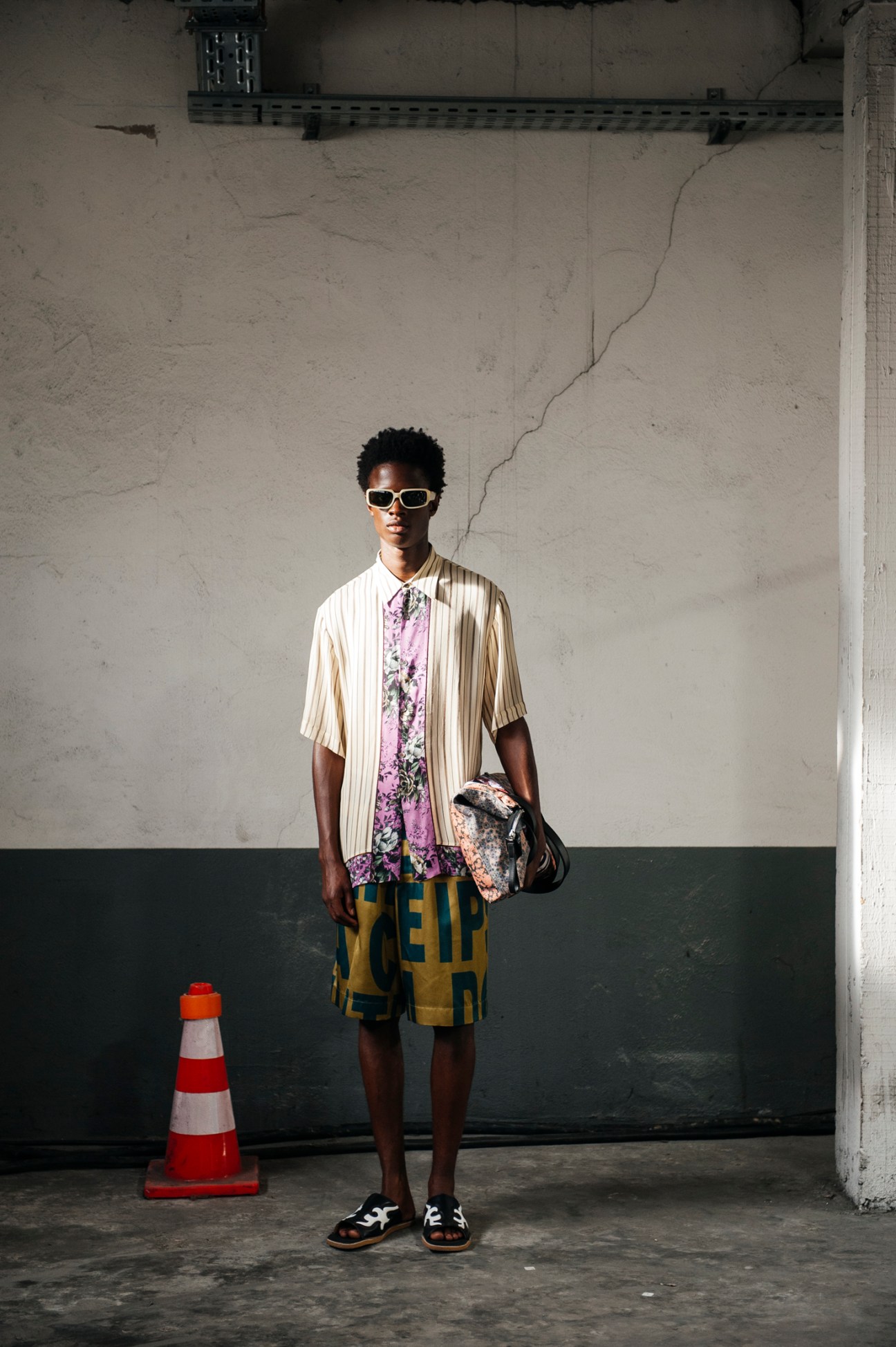 Model wearing layered Dries Van Noten menswear including striped shirt, floral print, and yellow shorts with sunglasses