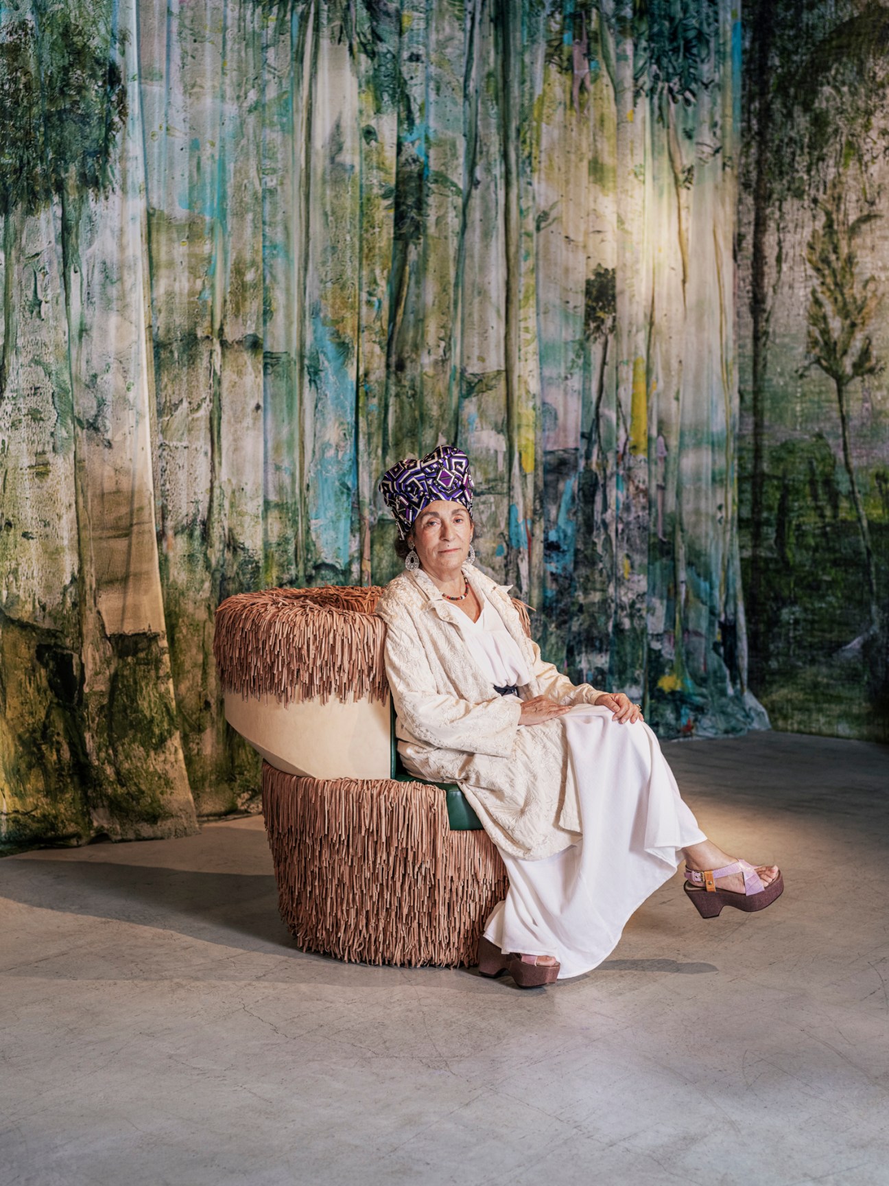 Nina Yashar sitting in a rounded leather Cha-cha lounge chair against vibrant patterned wallpaper