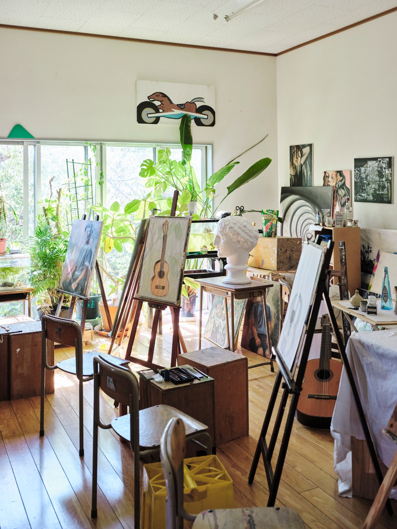 Artist's studio with easels, paintings, guitars, and plants near large windows in Porto.