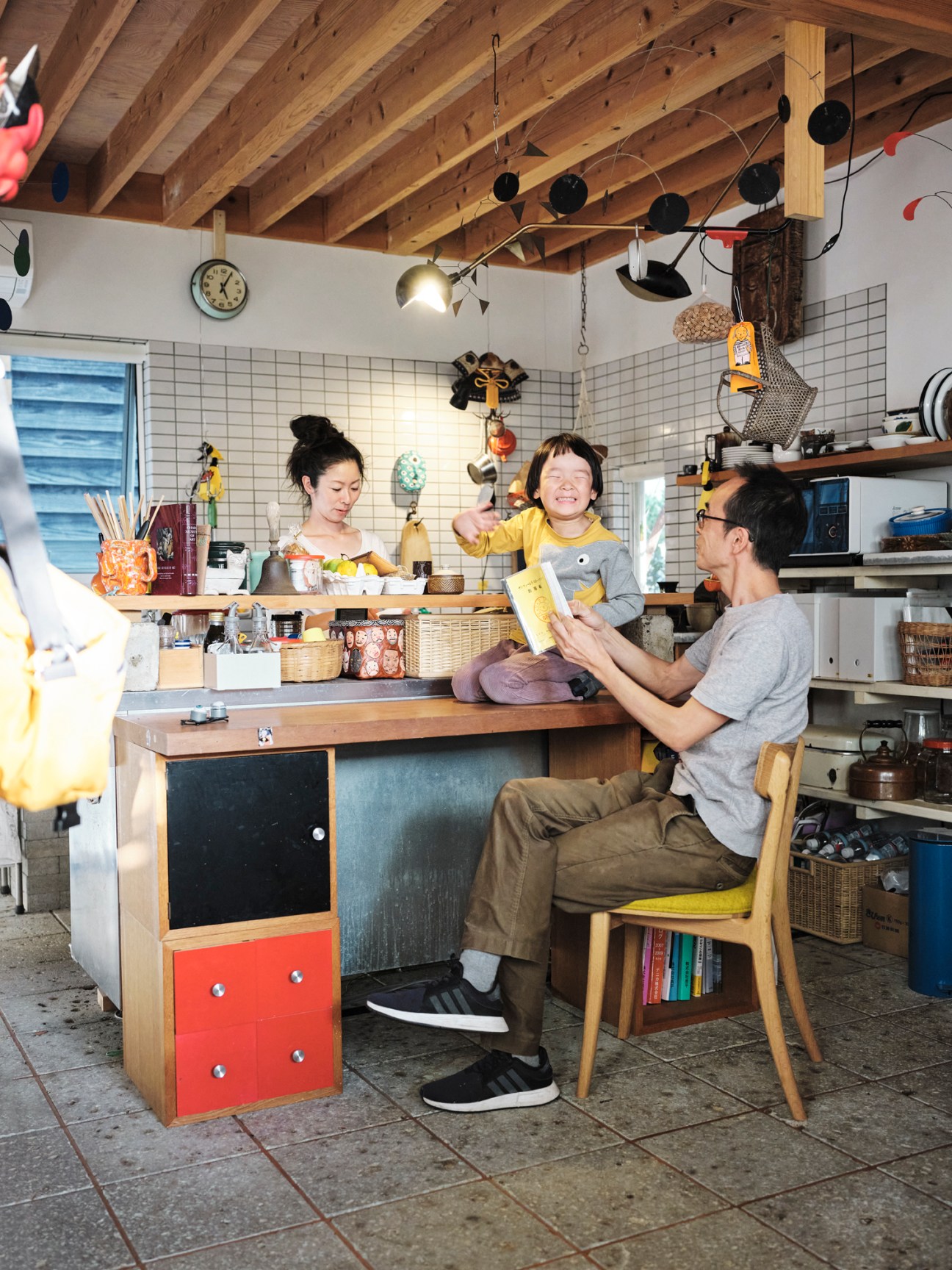 Family enjoying time together in a bright, eclectic kitchen with exposed wooden beams and hanging decorative items.
