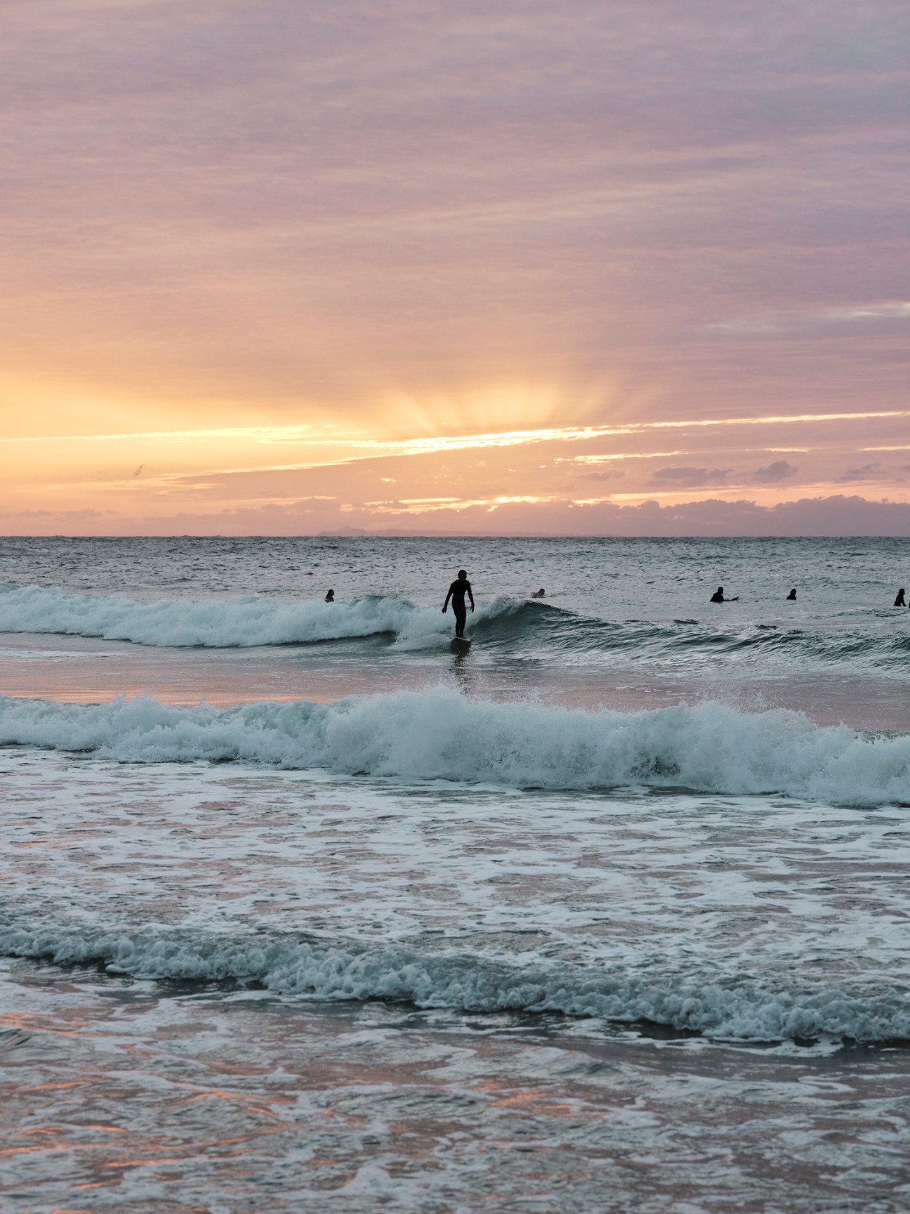 Surfers and swimmers in ocean waves at sunset on a beach in Itoshima, Japan.