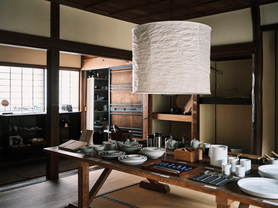Interior of traditional Japanese room with exposed wooden beams, tatami flooring, and table displaying pottery and tableware