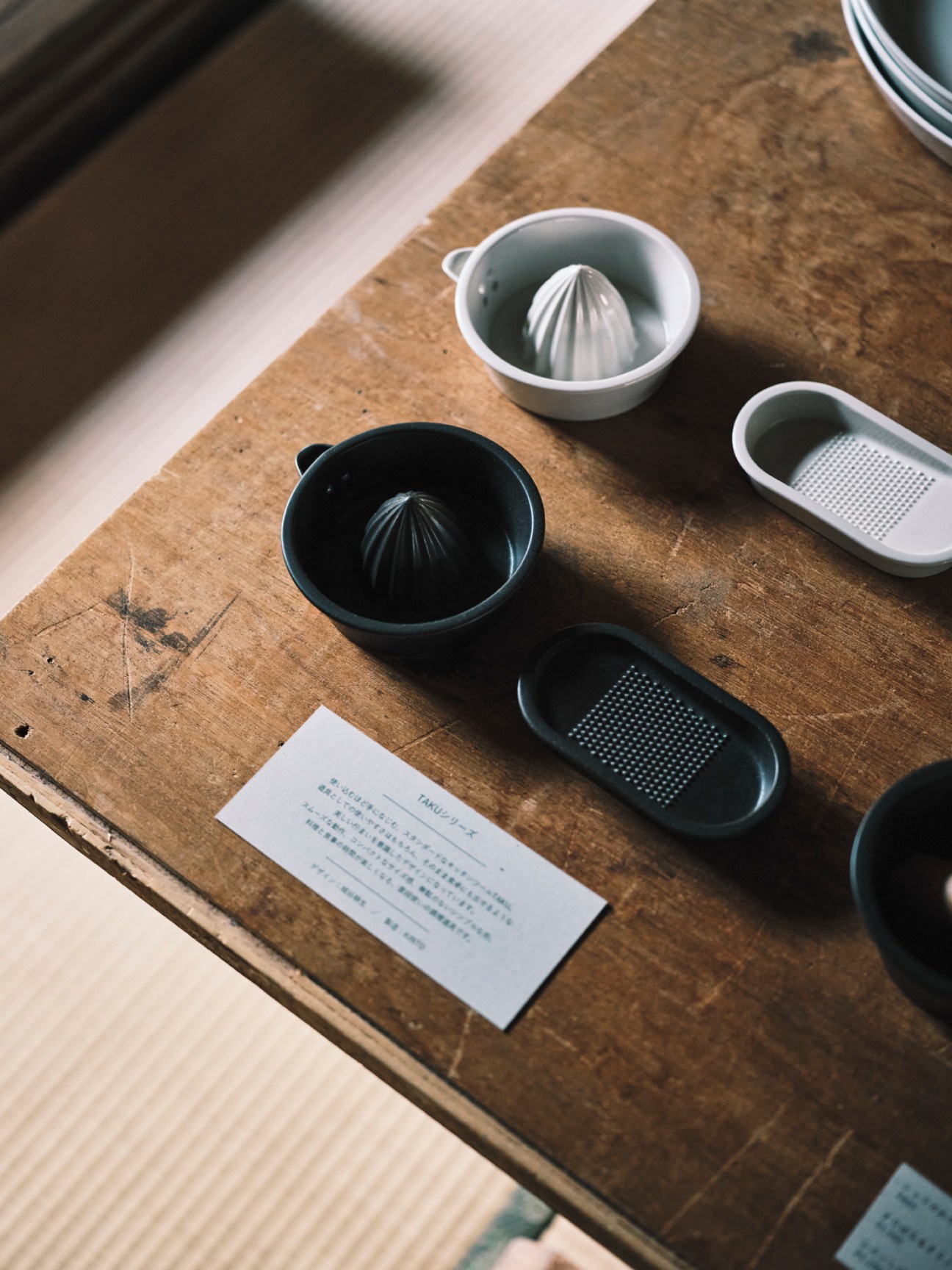 White and black ceramic bowls with citrus juicers and graters displayed on wooden surface