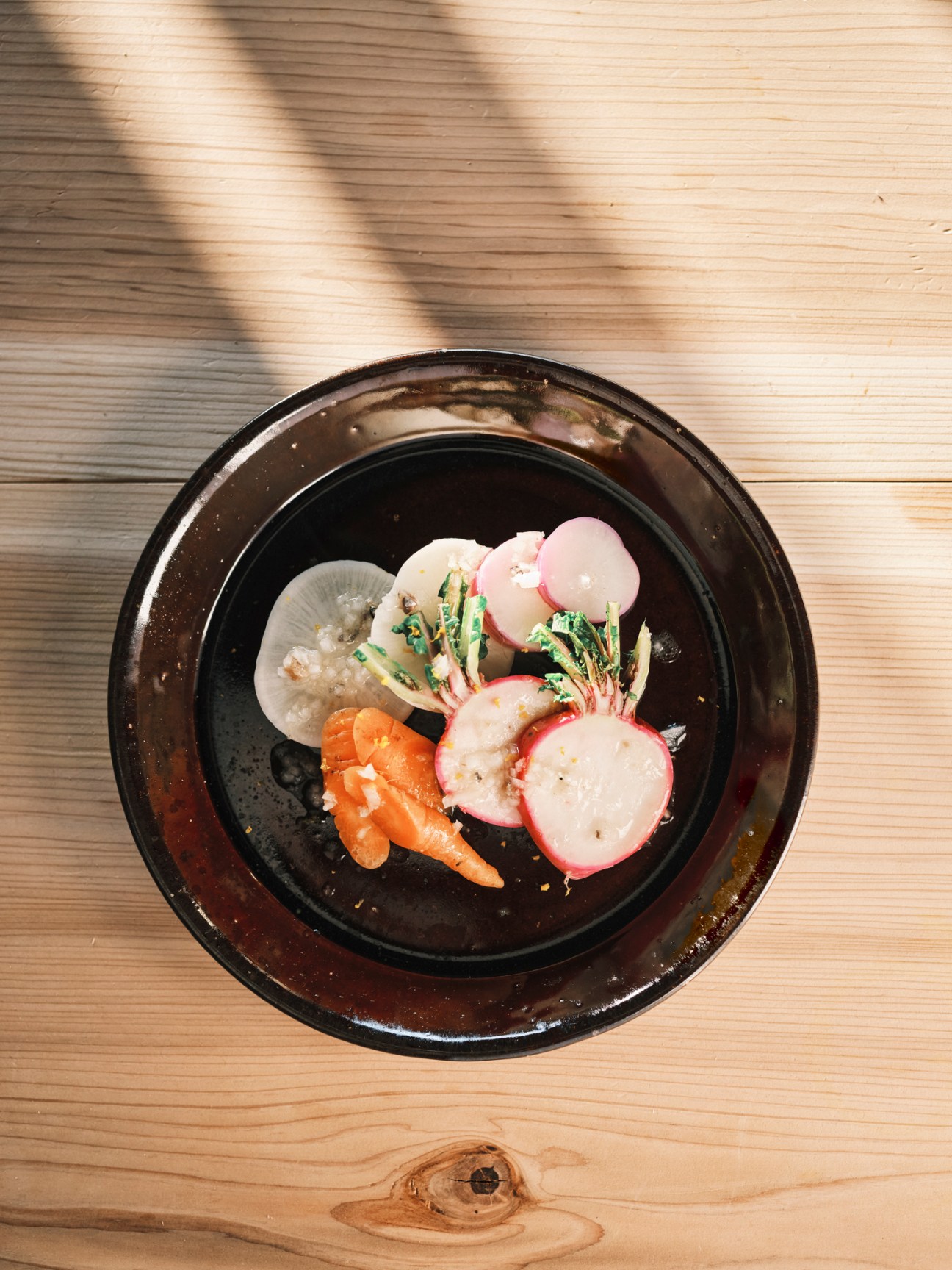 Elegant plated dish with thinly sliced radishes, citrus segments, and greens on a dark ceramic plate
