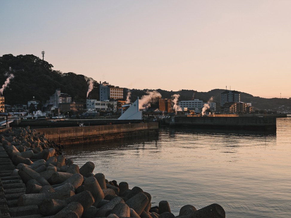 Harbor view of Obama town at sunset with industrial buildings, pier, and forested hills in background