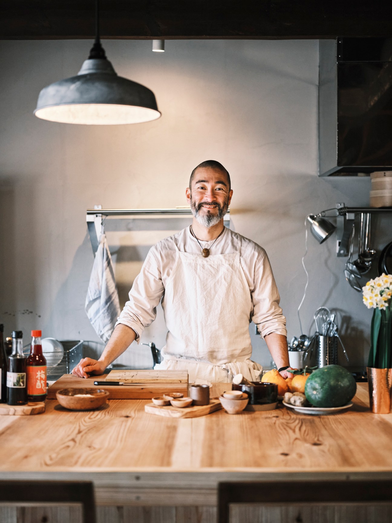 Chef Shinichiro Harakawa standing behind a wooden counter in his restaurant kitchen wearing white chef's attire