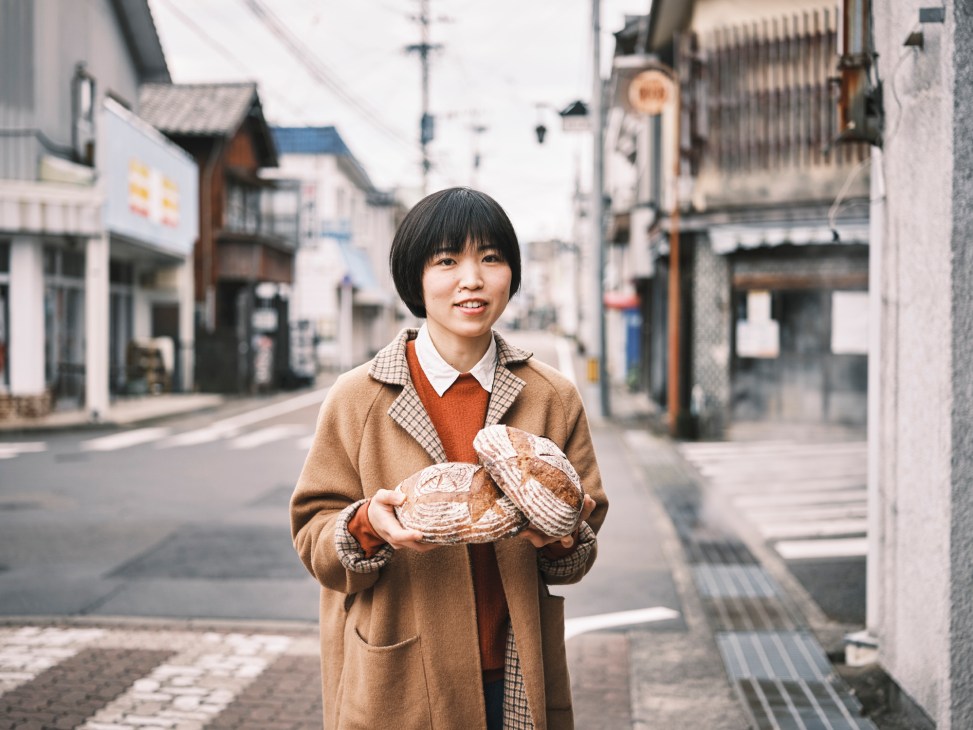 Baker Natsuko Hashimoto holding two round loaves of bread while standing on a street in traditional Japanese town