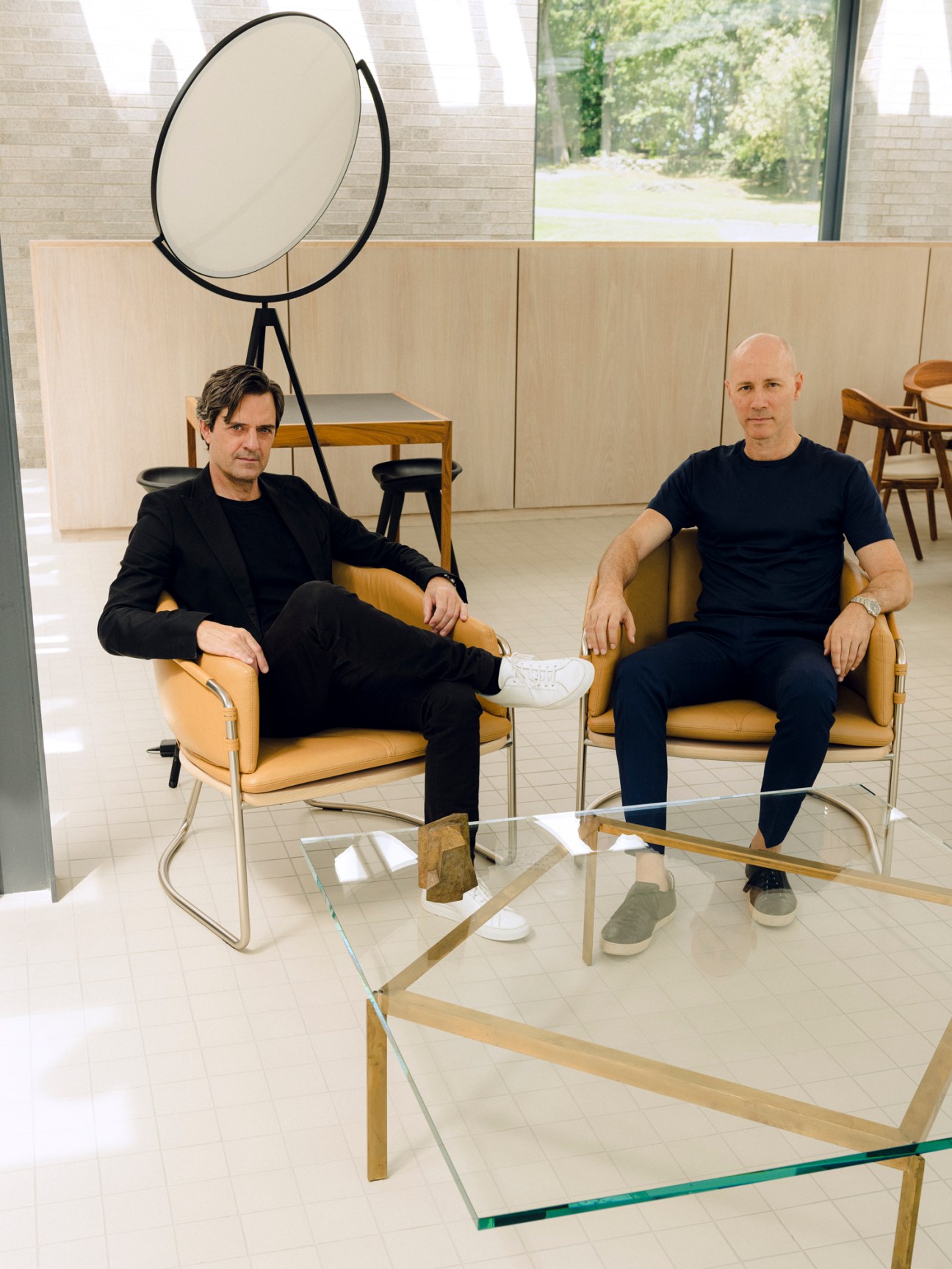 Two men seated in modern chairs in a minimalist office space with large windows and skylights.