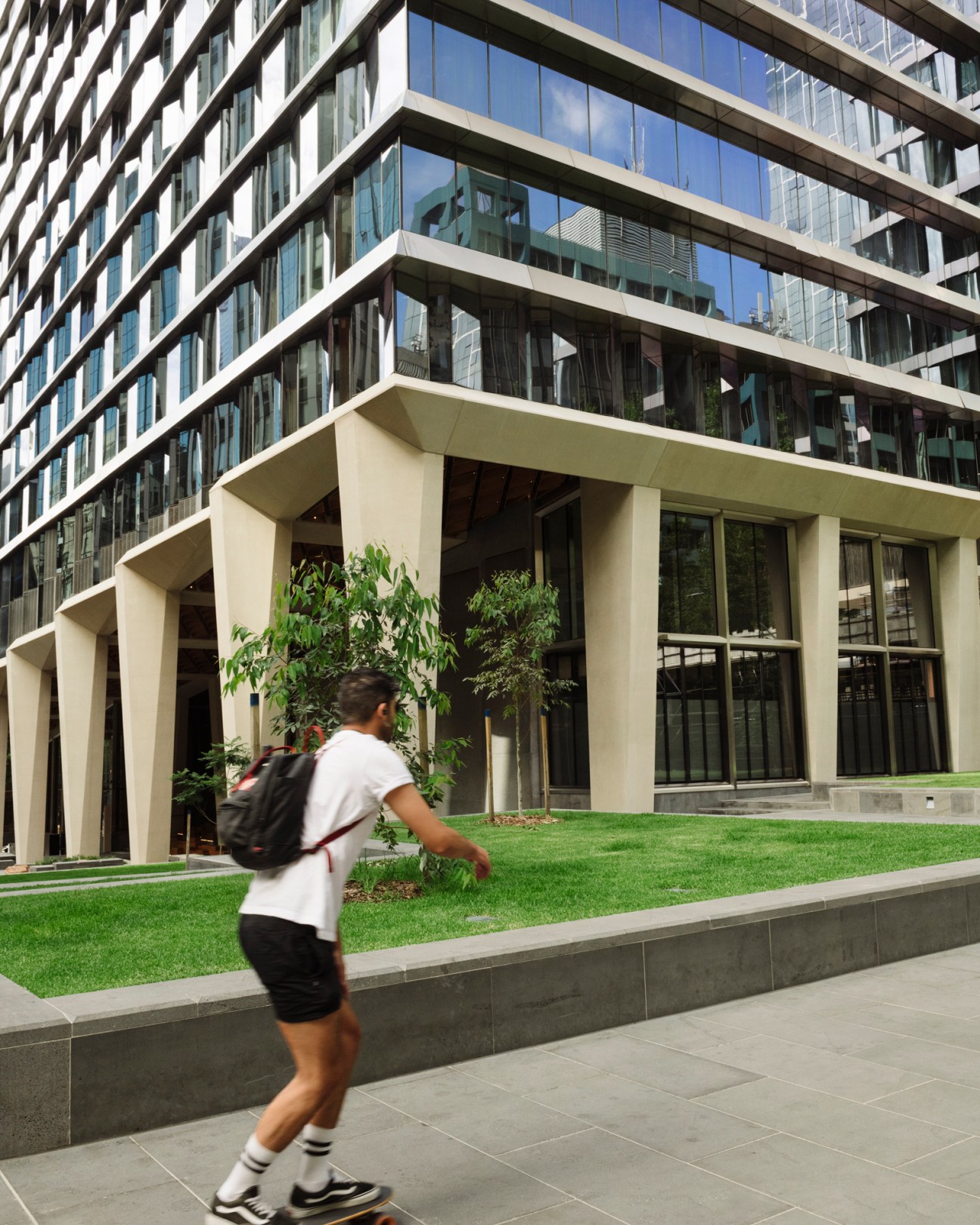 Person jogging past modern building with glass facade and landscaped green space