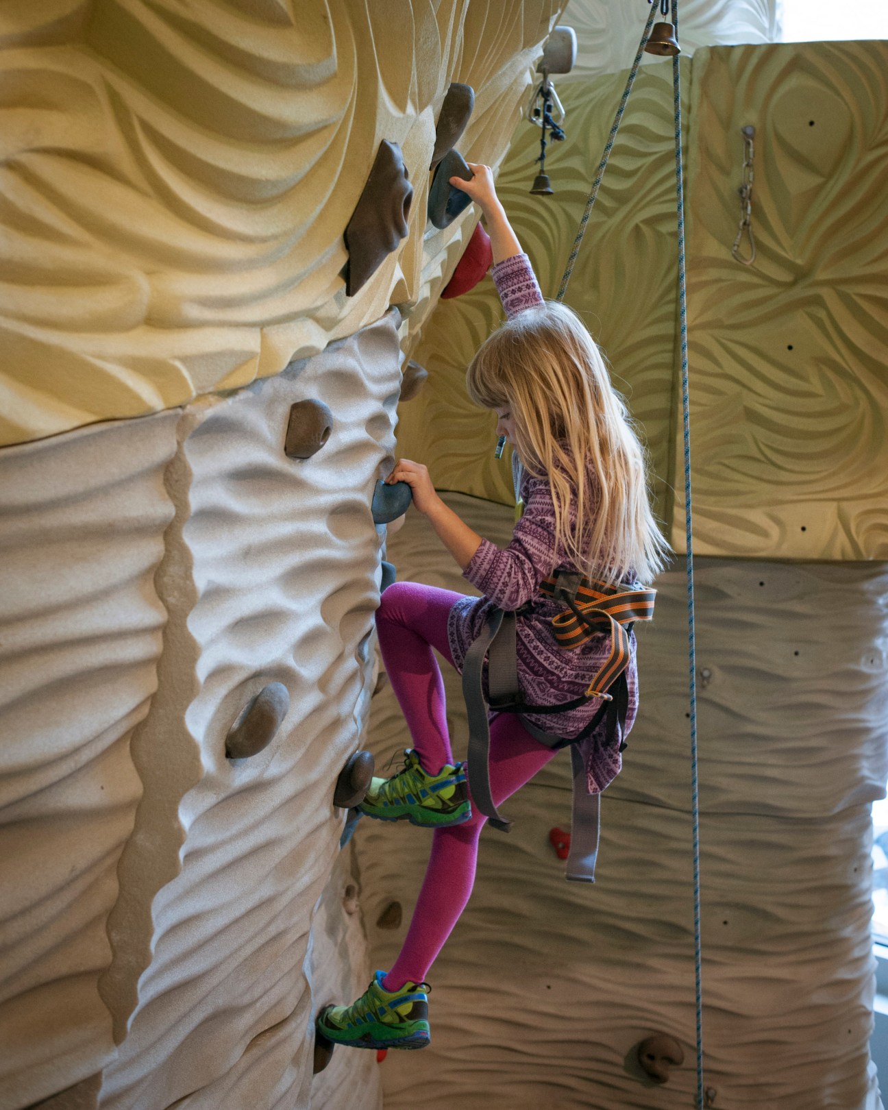 Child climbing indoor wall at Sporthaus Schuster with safety harness and ropes.