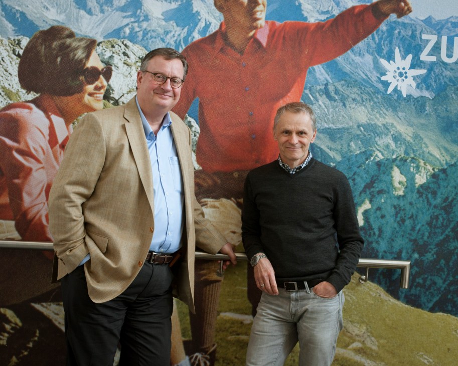 Flori Schuster and co-CEO Rainer Angstl stand in front of a vintage alpine tourism poster at Sporthaus Schuster in Munich.