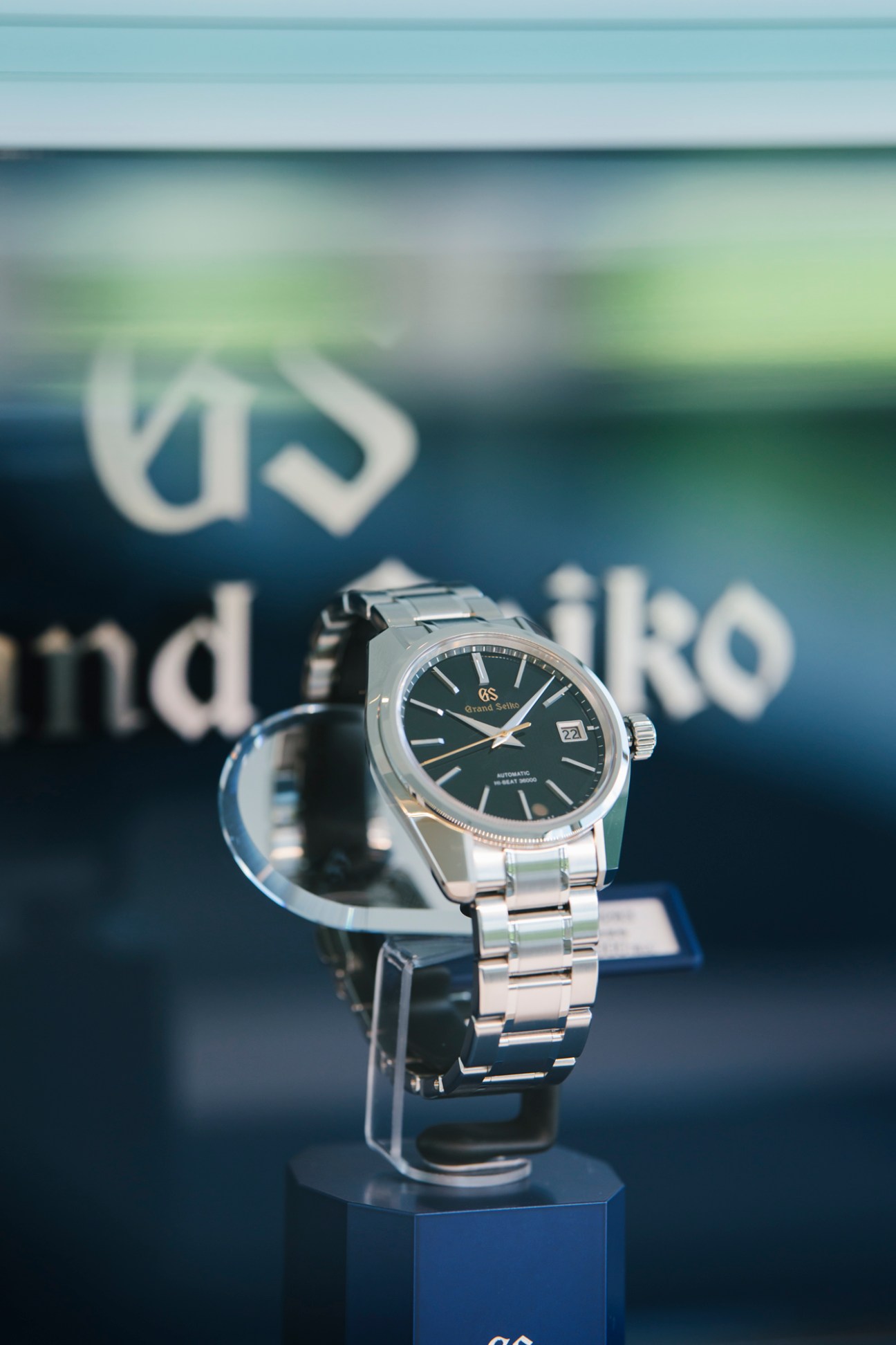 Grand Seiko Mechanical Hi-Beat 36,000 watch with dark dial and steel bracelet displayed on clear stand