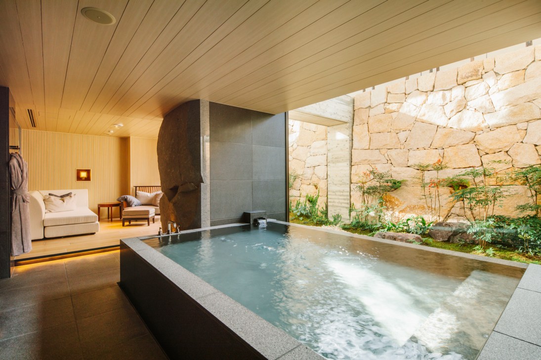 Luxury hotel spa room with wooden ceiling, stone walls, rectangular hot spring pool and seating area