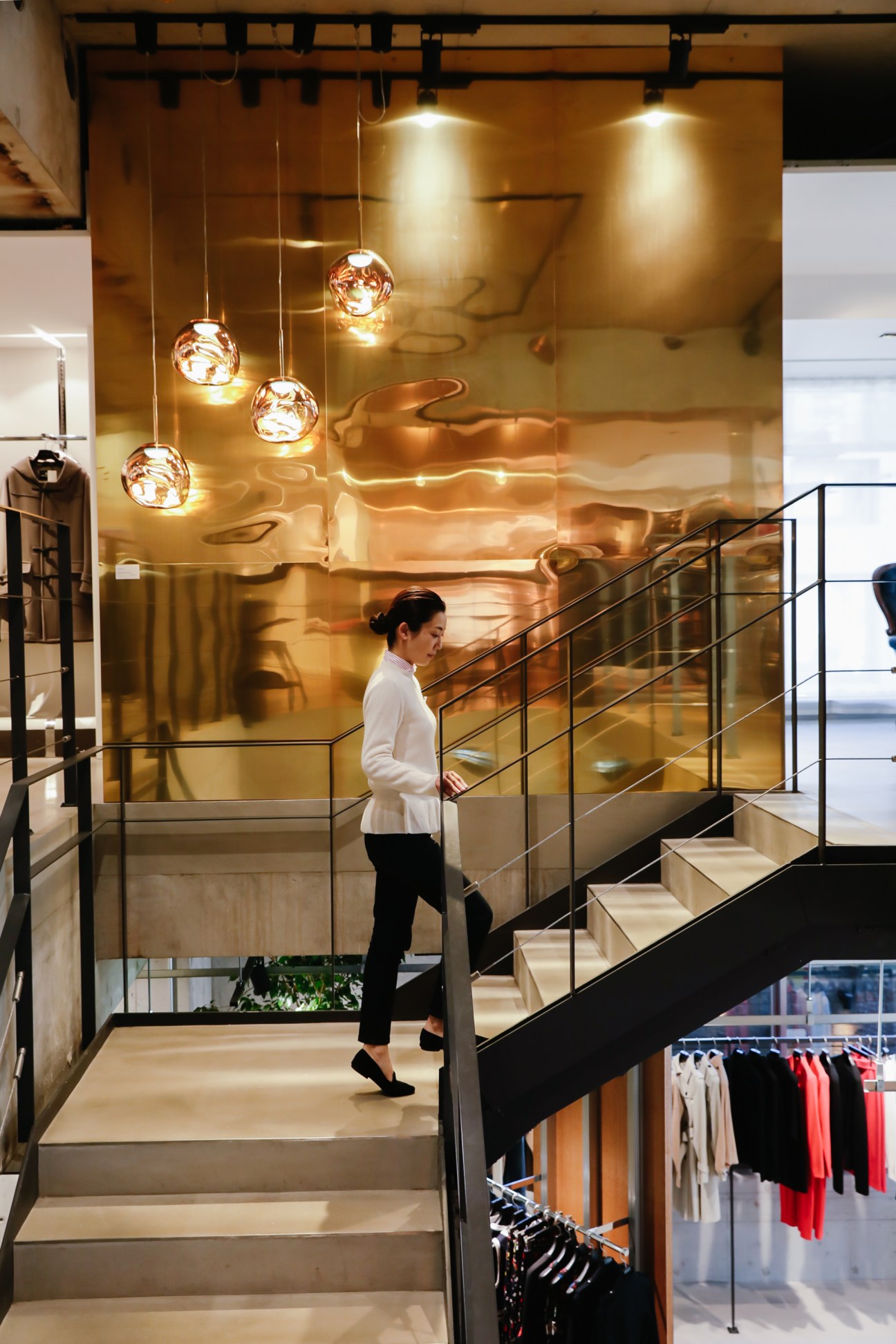 Woman in white jacket walking down modern staircase in contemporary retail interior with pendant lighting