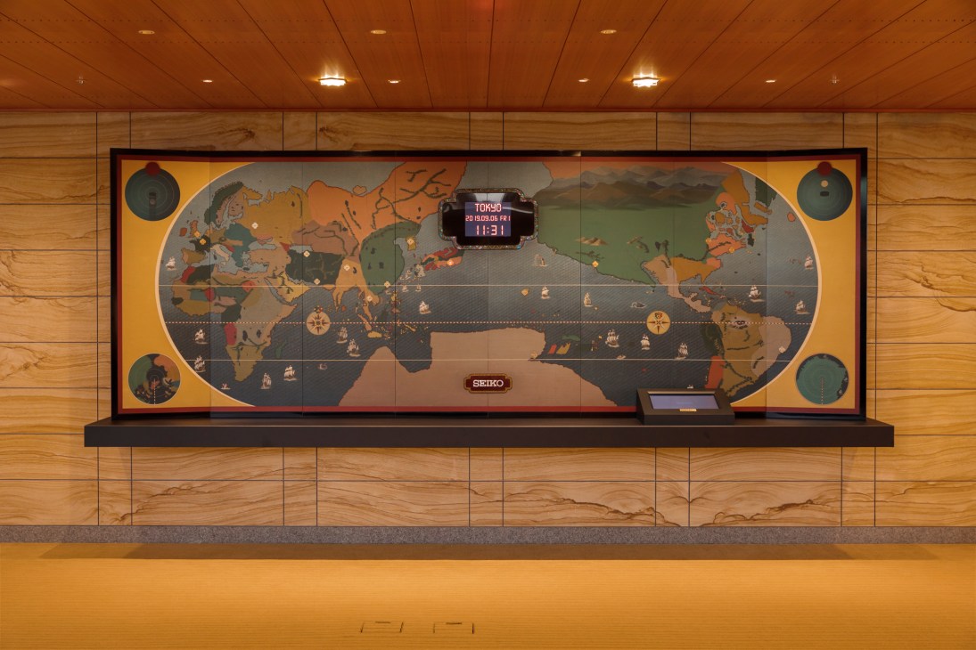Large vintage world map clock mounted on wood-paneled wall showing multiple time zones with digital display