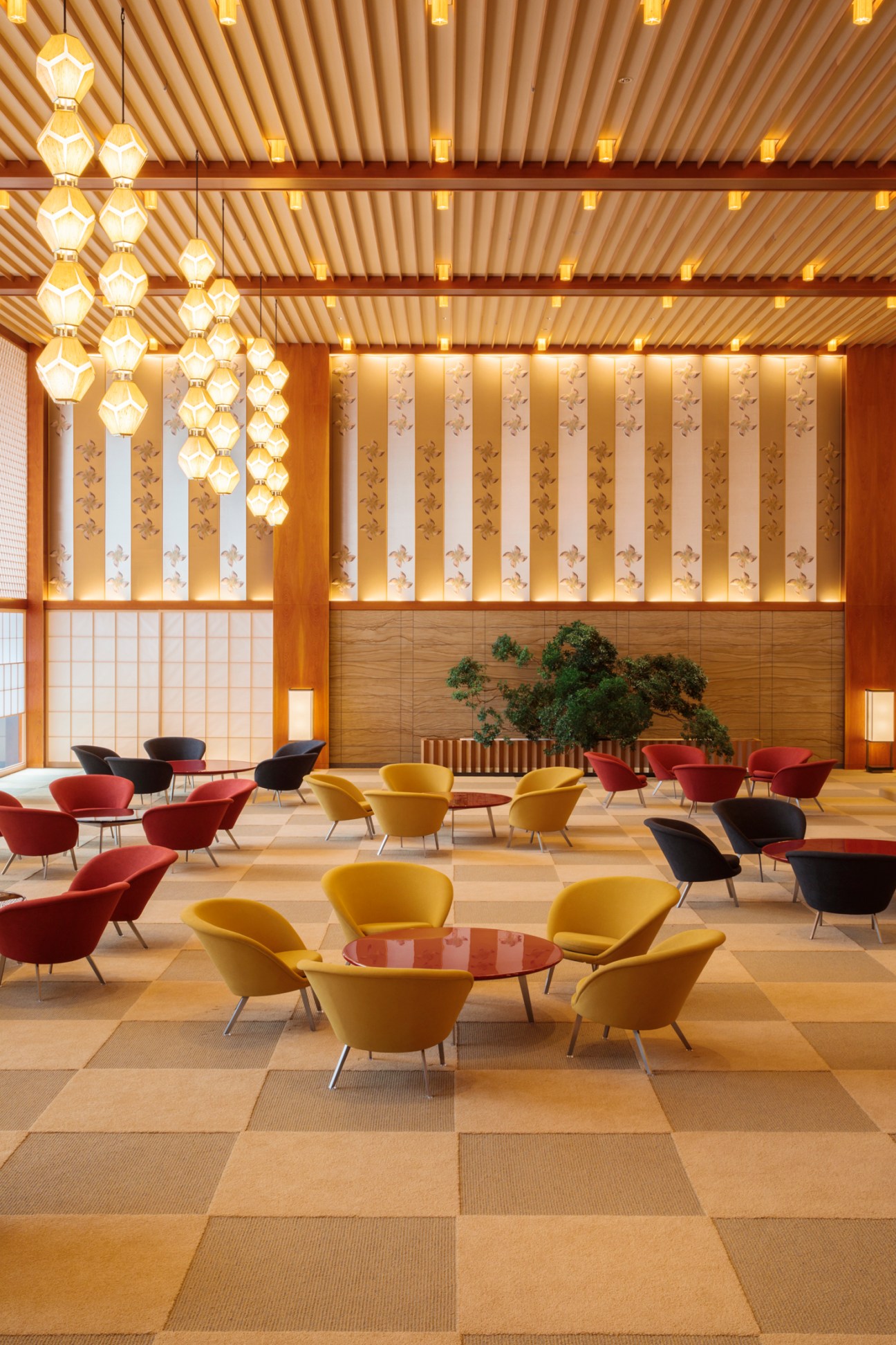 Modern hotel lobby with geometric hexagonal light fixtures, colorful armchairs around small tables, and wood ceiling