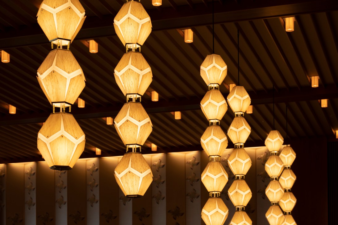 Geometric pendant lights with golden wooden panels and brass fittings hang from a dark wooden ceiling