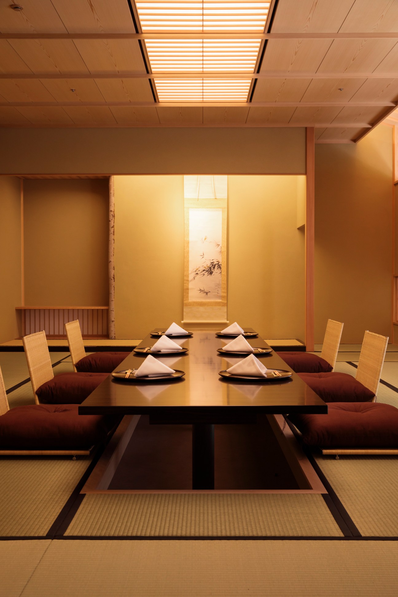 Traditional Japanese dining room with low wooden table, floor cushions, tatami mats, and hanging scroll artwork