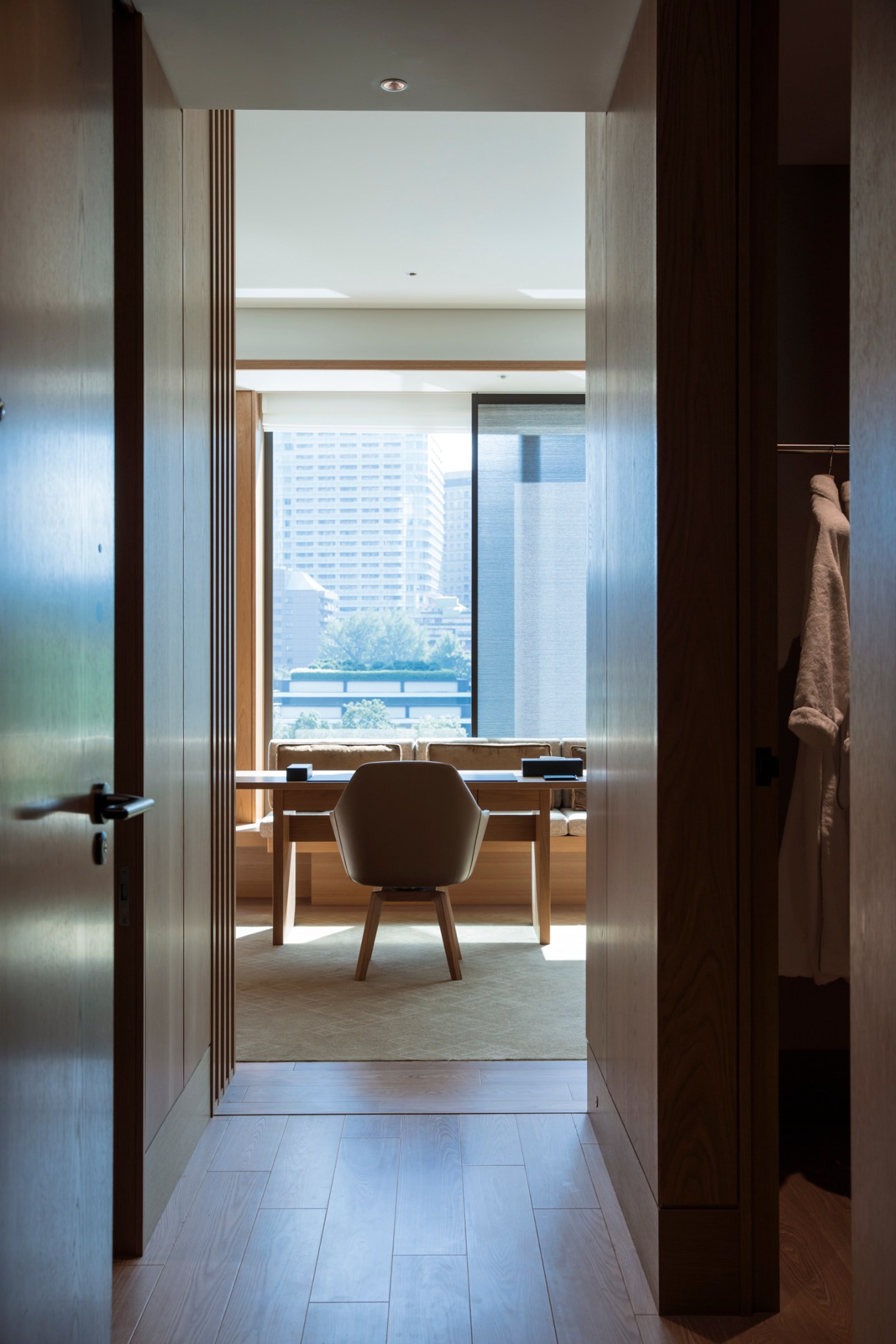 View through hotel room doorway showing modern desk and chair with Tokyo cityscape visible through large window