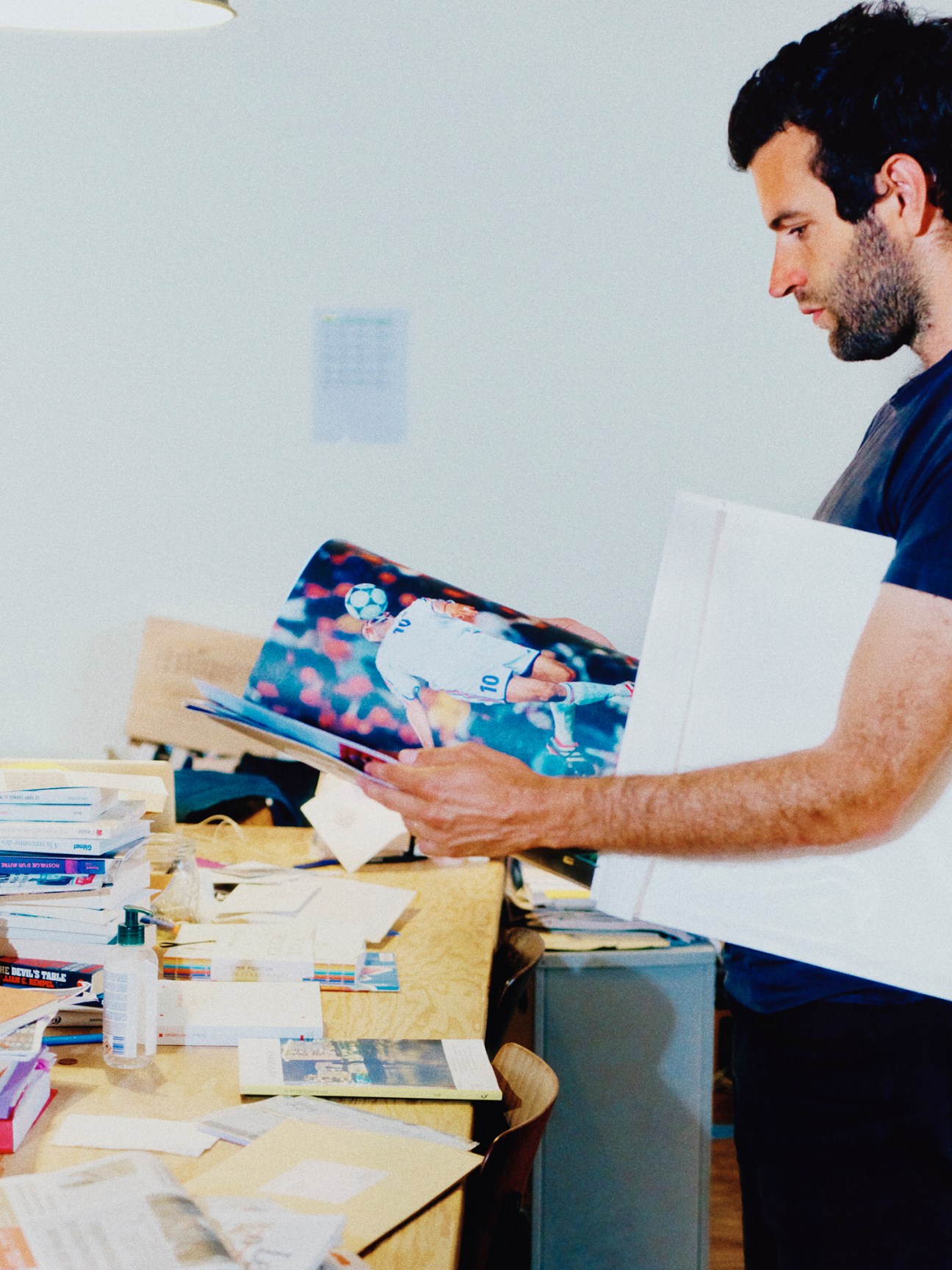 Person reading a colorful magazine spread at a desk with papers and books scattered around