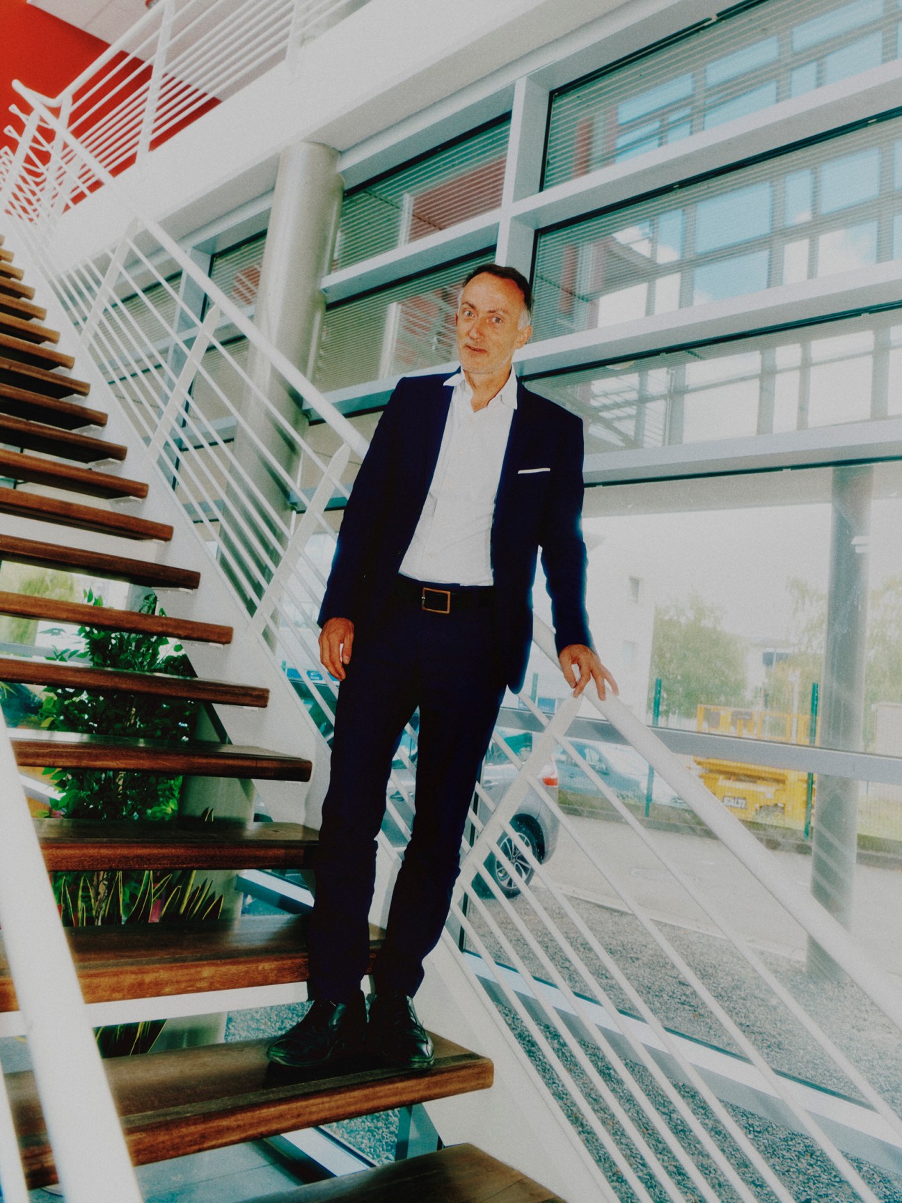 Etienne Vervaecke standing on modern staircase in contemporary building with large windows wearing a dark suit and white shirt