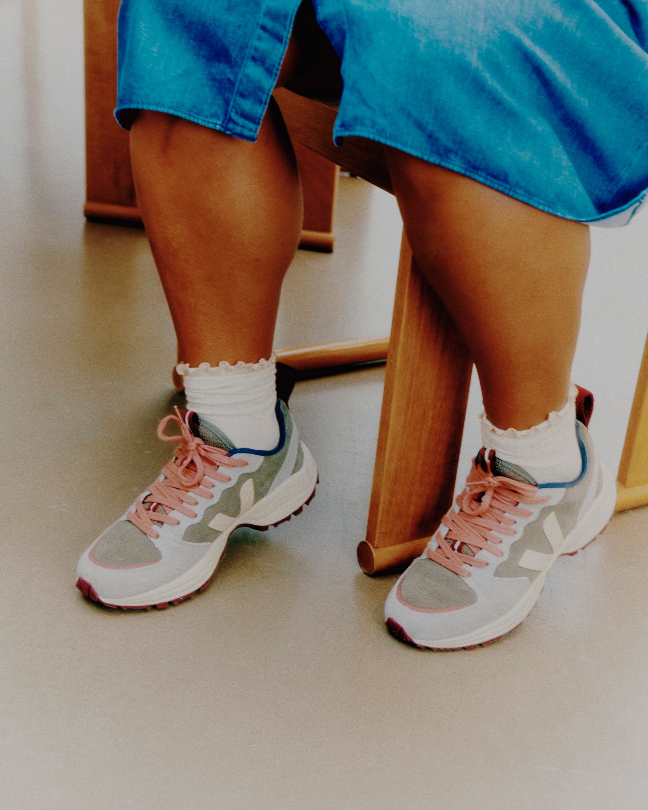 Person wearing blue jeans and white Veja sneakers with pink laces and colorful V logo accents