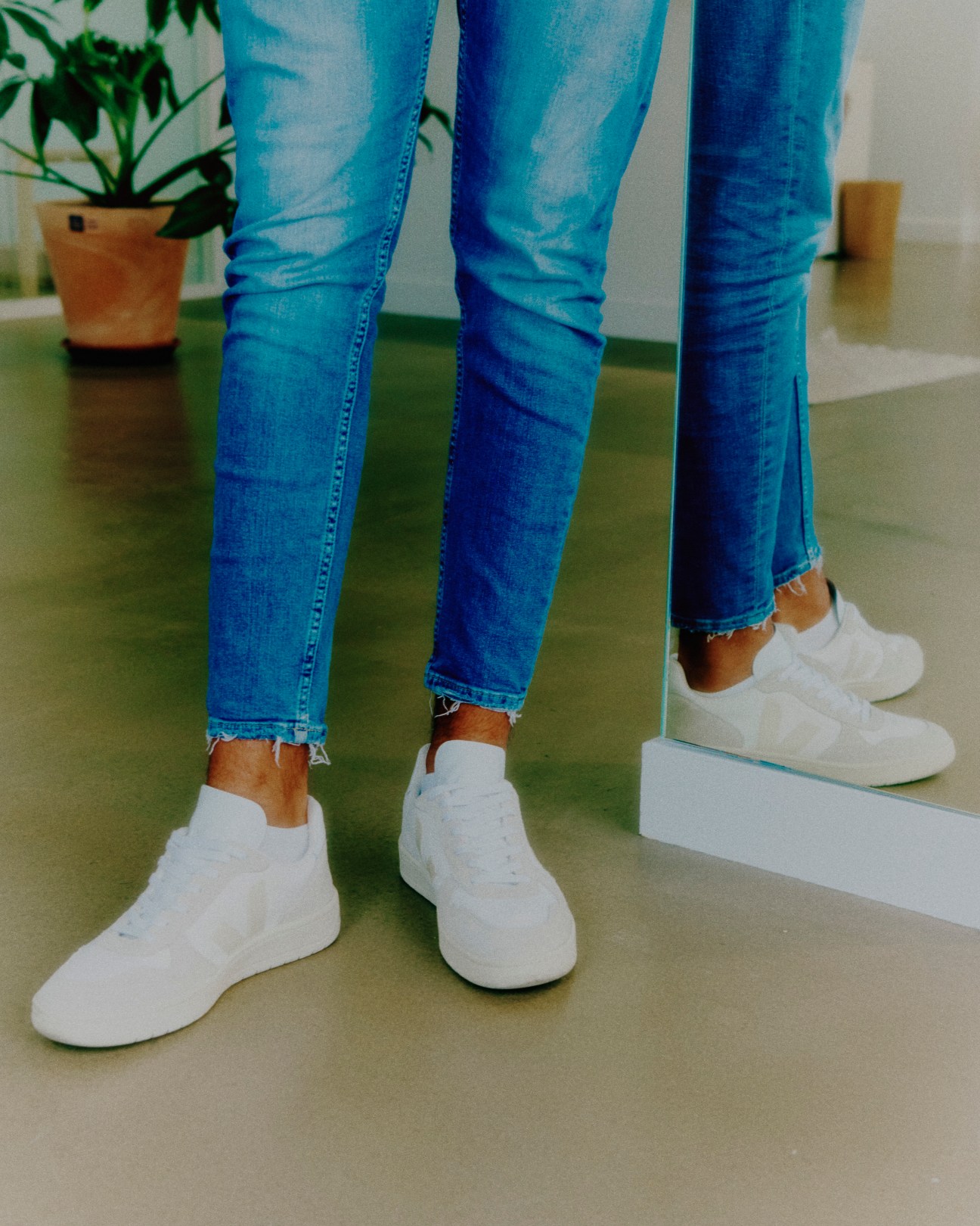 Person wearing blue jeans and white sneakers standing next to mirror