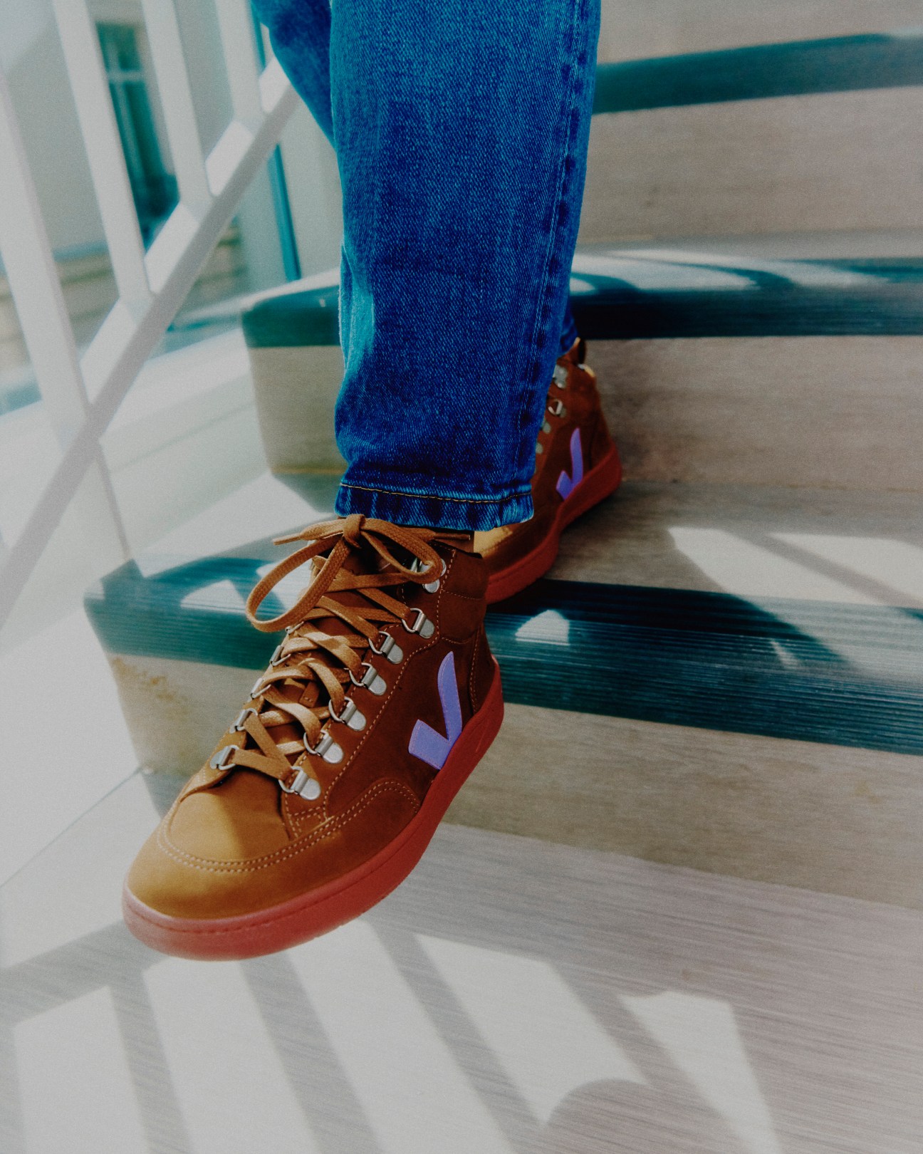 Person wearing brown Veja sneakers with purple V logo and blue jeans on white geometric floor