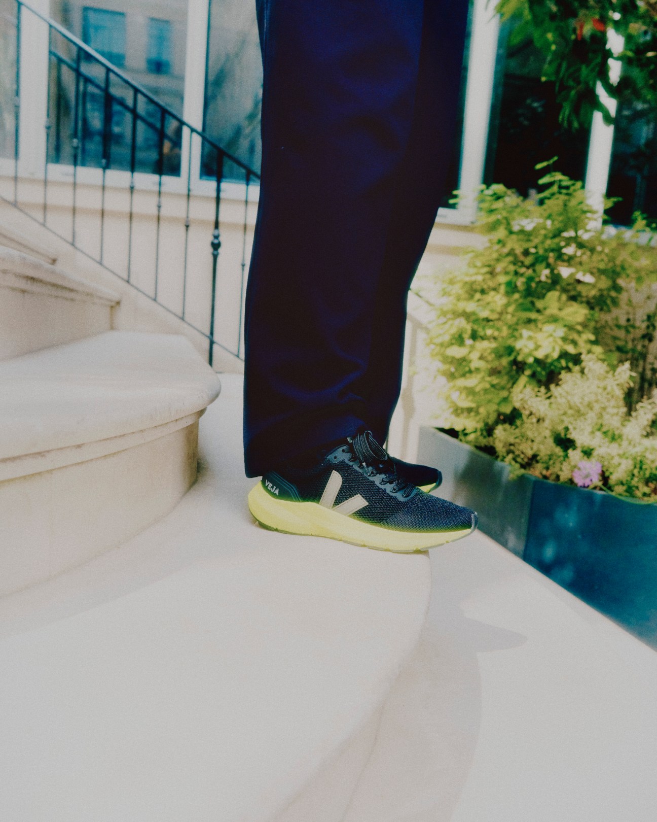 Woman with long brown hair wearing dark clothing on white stairs with Veja sneakers