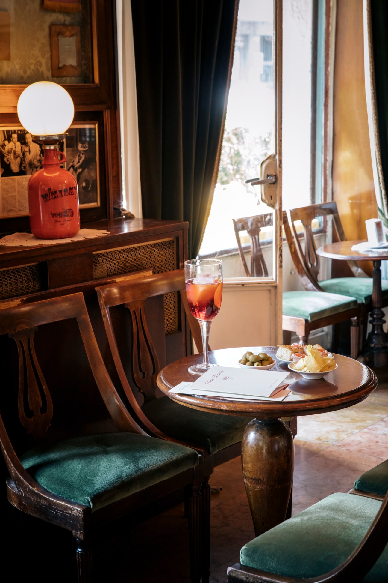 Aperitivo setup with wine glass, small plates of olives and appetizers on wooden table in elegant restaurant interior