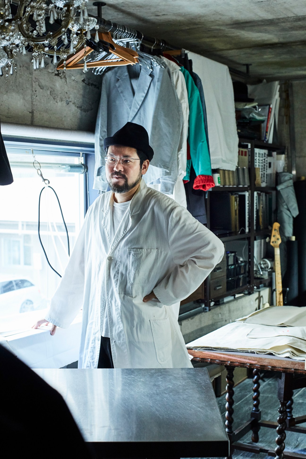 Designer Kensuke Hoshi in his Tokyo atelier surrounded by garments on hangers and tailoring materials.
