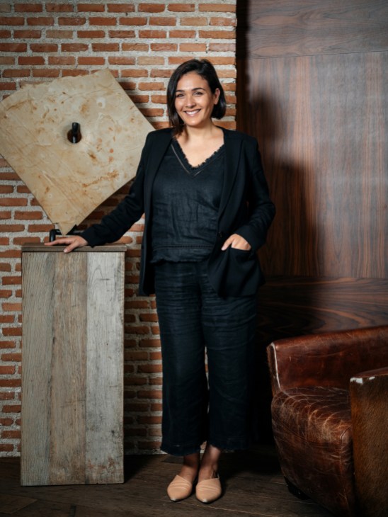 Adriana Domínguez, CEO of Adolfo Domínguez, poses with wooden design pieces in a studio setting.