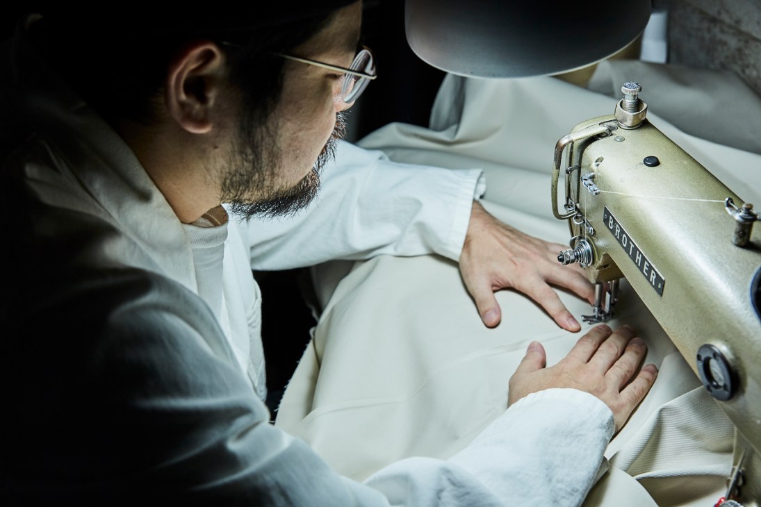 Designer Kensuke Hoshi sewing a cream-coloured garment on a Brother sewing machine in his Tokyo atelier.