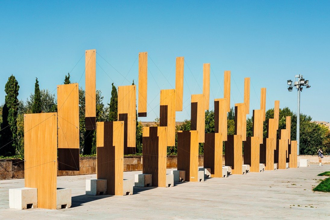 Orange wooden arched structures arranged in rows on concrete plaza with trees in background