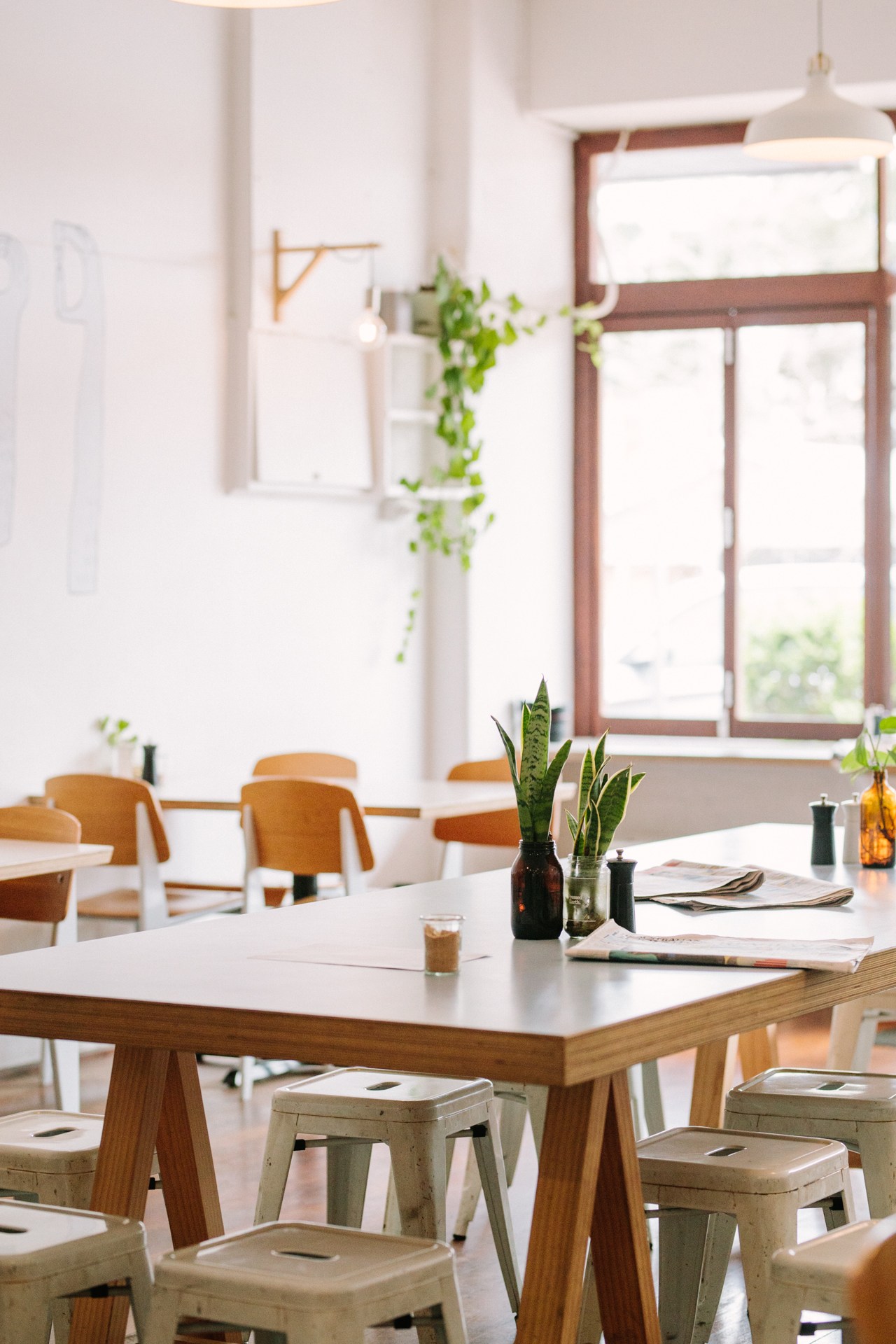 Bright, minimalist café interior with wooden tables, ochre chairs, potted plants, and sunlit windows at Good Things in Perth.