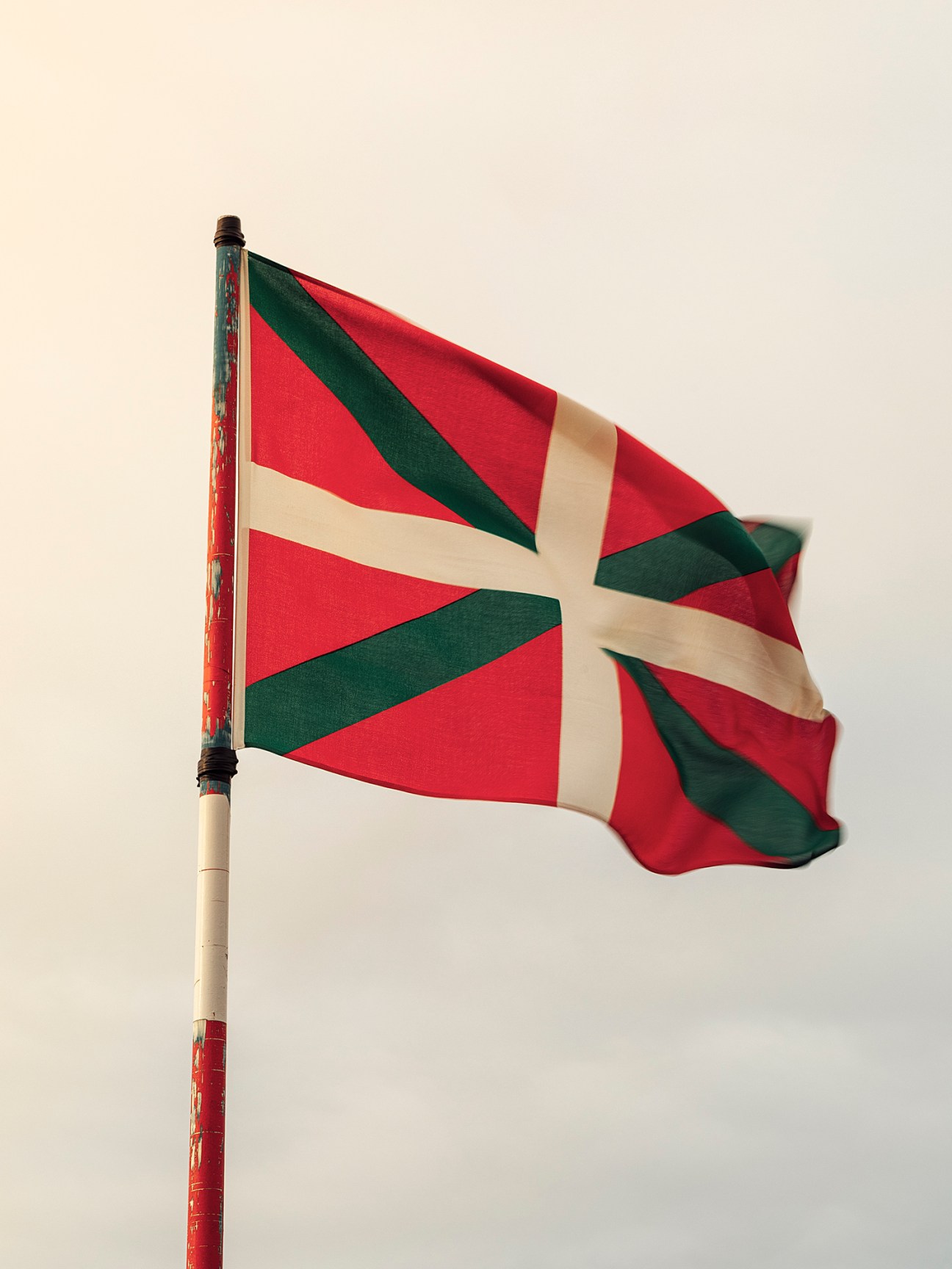 Red and white Basque Country flag with green cross patterns waving on a pole