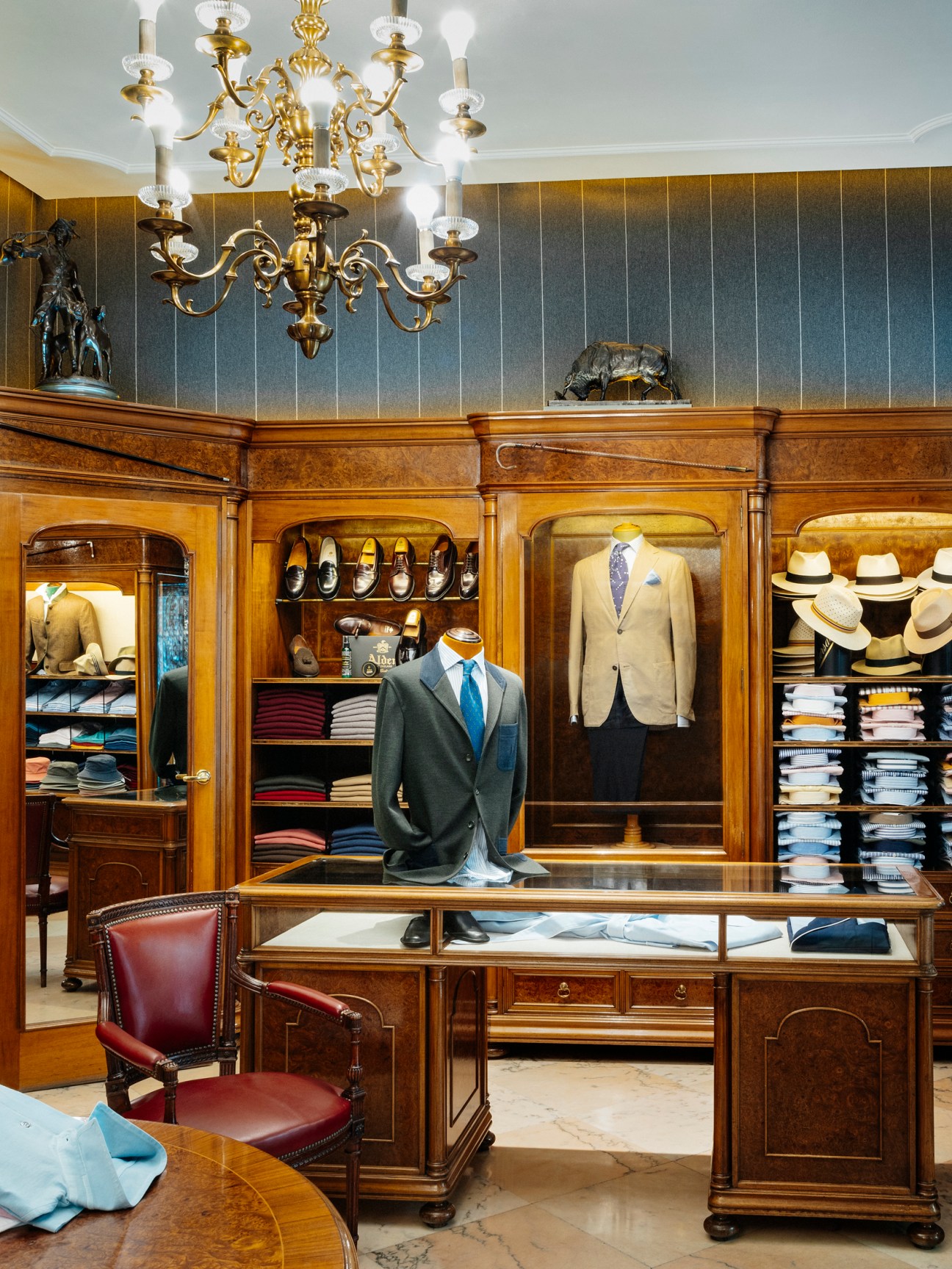 Elegant menswear boutique interior with wooden fixtures, suits on display, and ornate chandelier