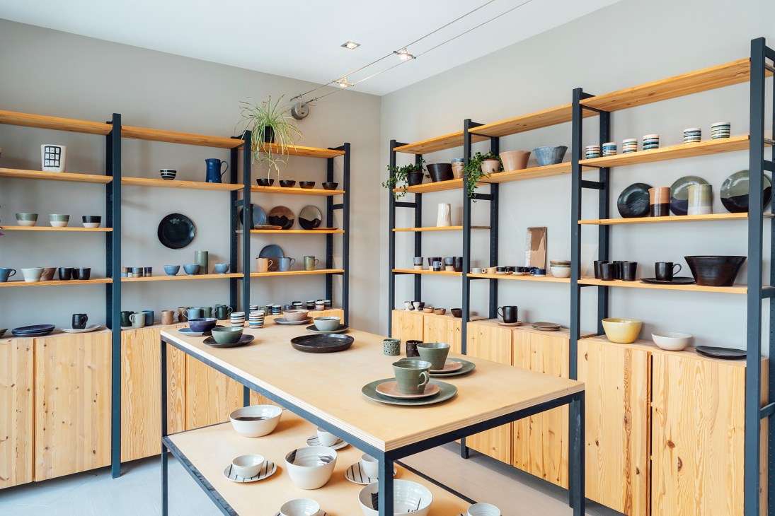 Ceramicist Lena Baltazard's pottery workshop with shelving displaying handmade ceramic bowls, cups, and tableware in various colors and finishes.
